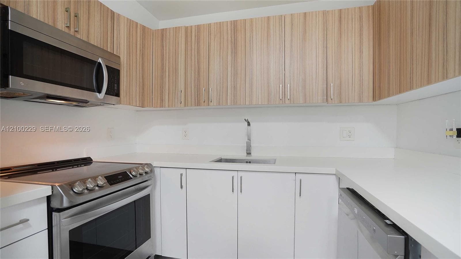 Kitchen featuring light wood-finish cabinetry, solid white countertops, stainless steel appliances, and a single-basin sink