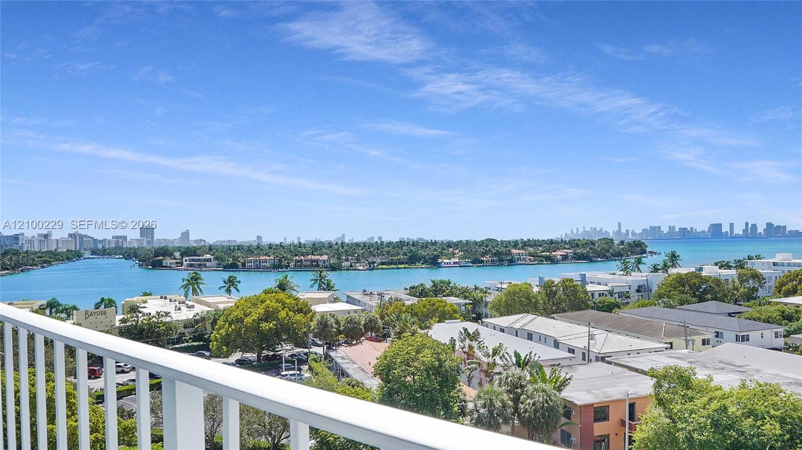 Elevated terrace with a white metal railing overlooking a waterfront expanse, coastal landscape, and a distant city skyline