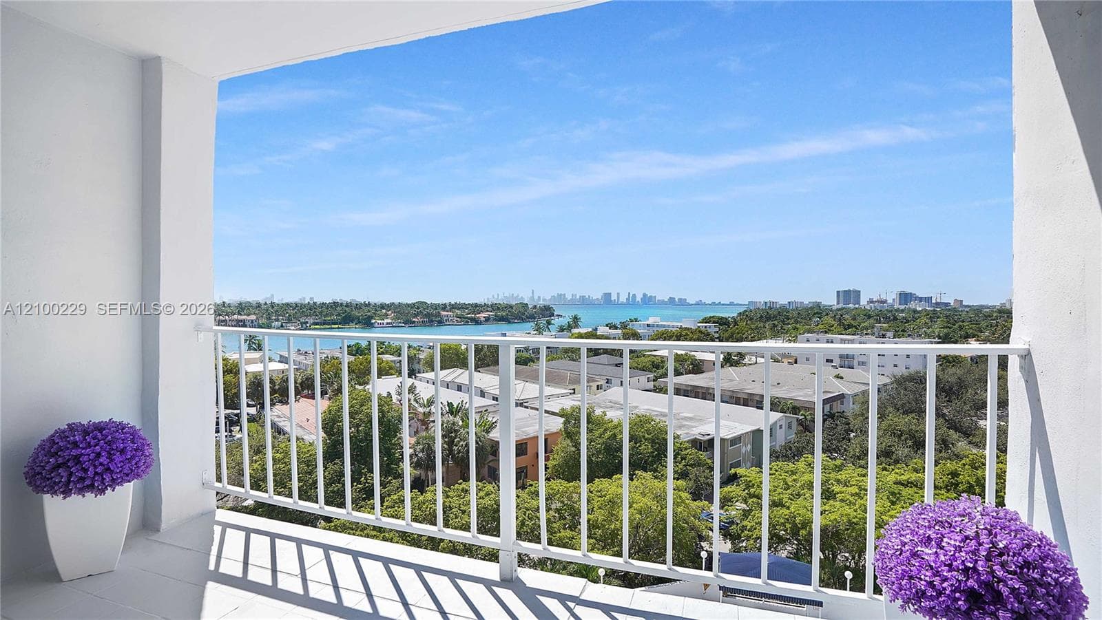 Covered balcony featuring a white metal railing and tile flooring, showcasing water and cityscape surroundings