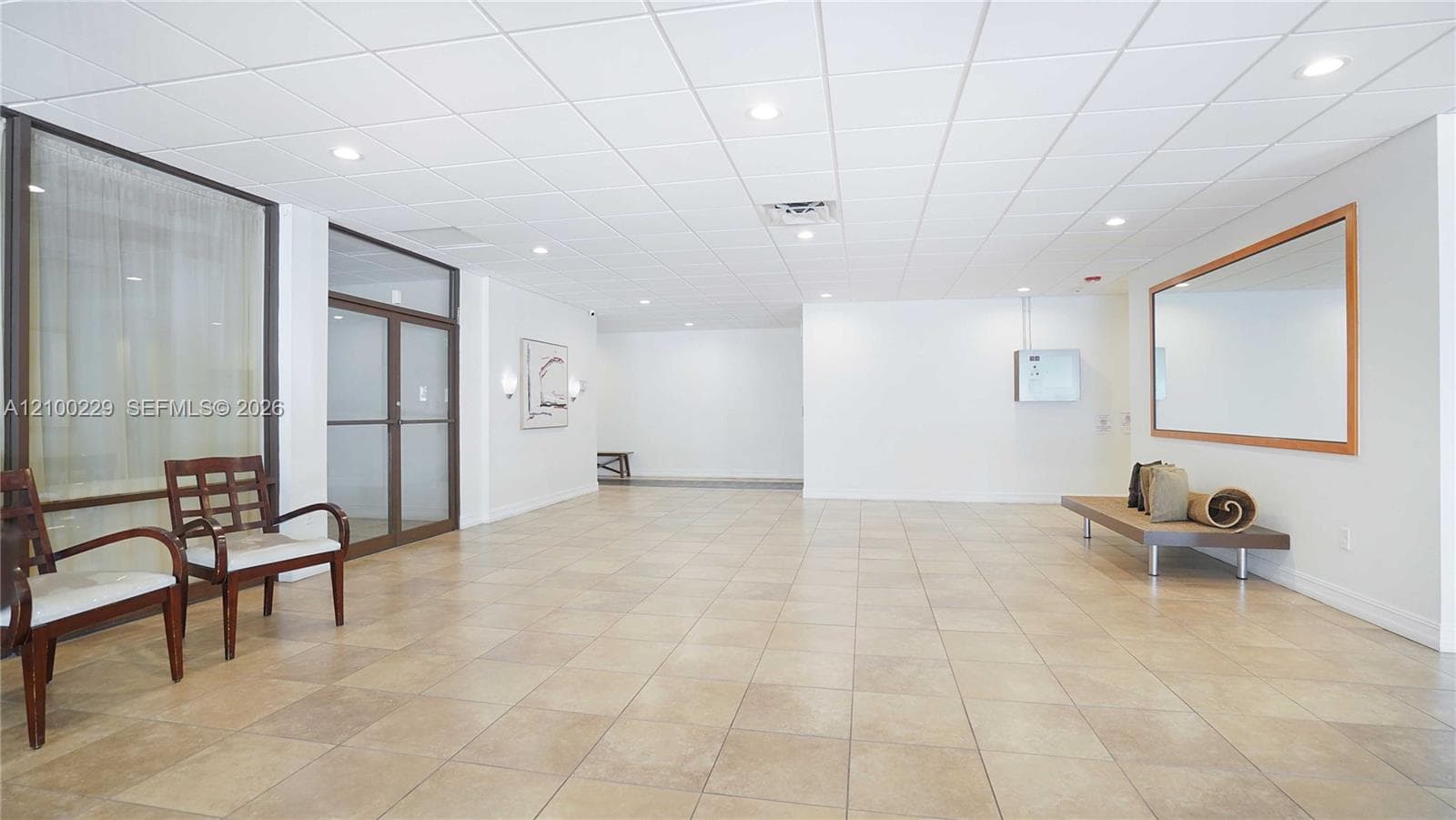 Spacious interior featuring large-format tile flooring, a drop ceiling with recessed lighting, and a substantial wall-mounted mirror with a wood-tone frame