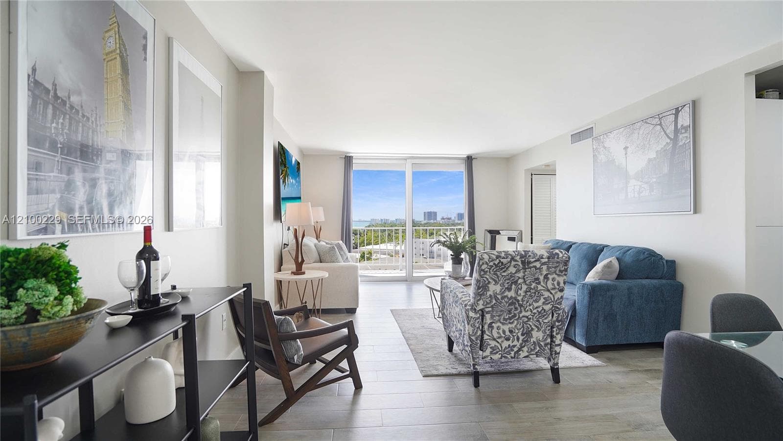 Open-concept interior featuring light wood-finish tile flooring, neutral wall tones, and floor-to-ceiling glass sliding doors leading to a balcony