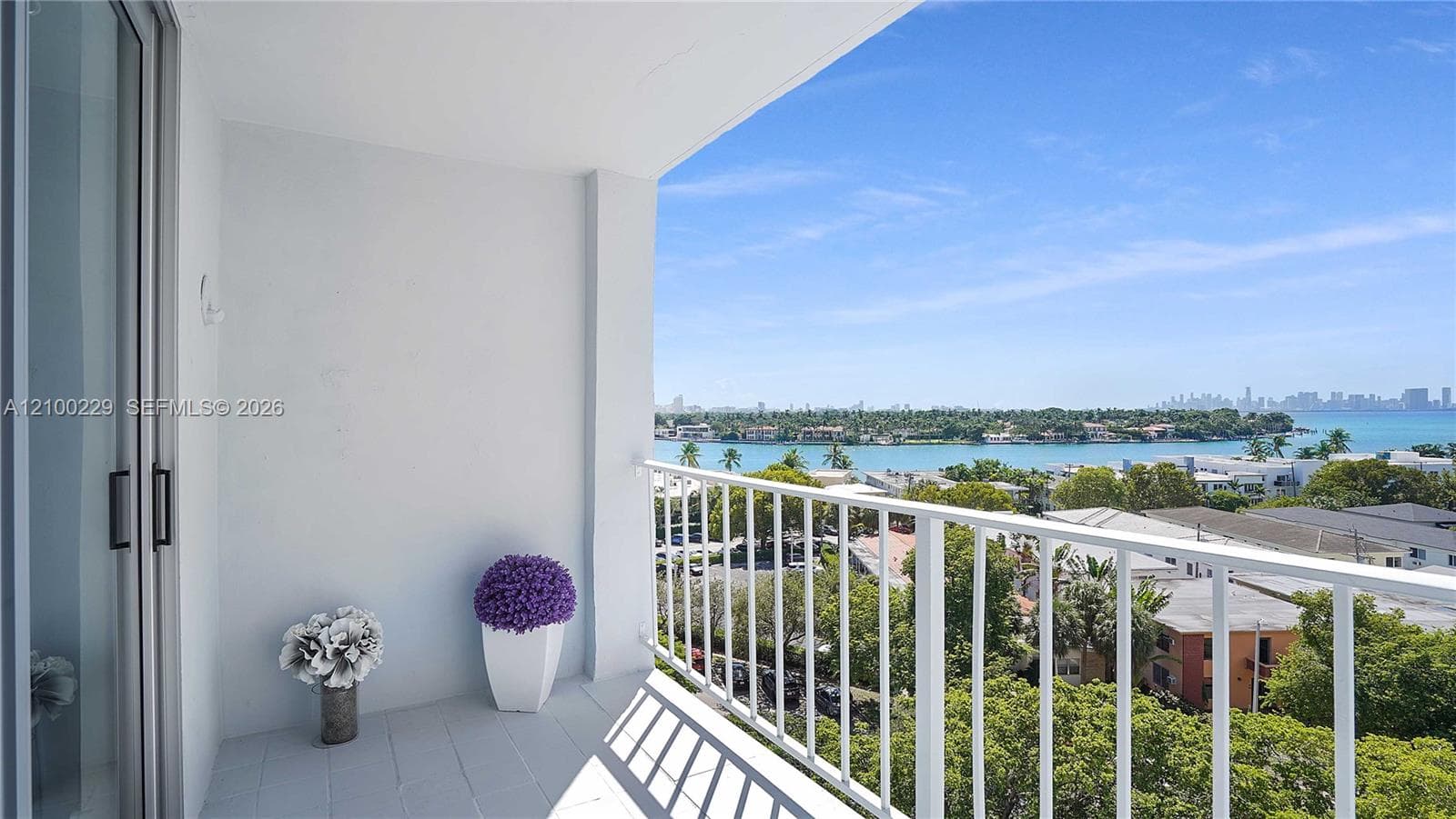 Covered balcony featuring tile flooring and a white metal railing, overlooking the water and metropolitan skyline