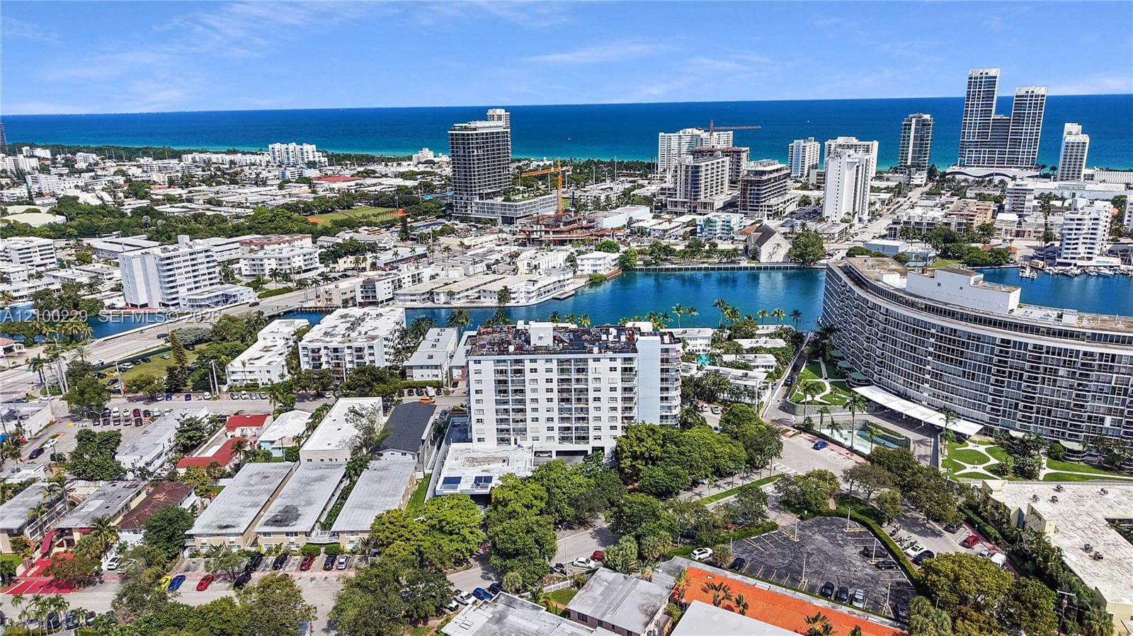 Aerial perspective of coastal urban environment featuring multiple high-rise structures, proximity to open water, and mature tree-lined surroundings