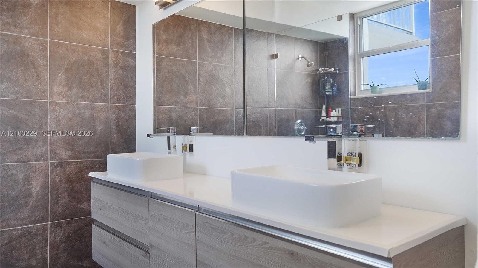 Floating wood-finish double vanity with rectangular vessel sinks, expansive wall-to-wall mirror, and large-format tile surround