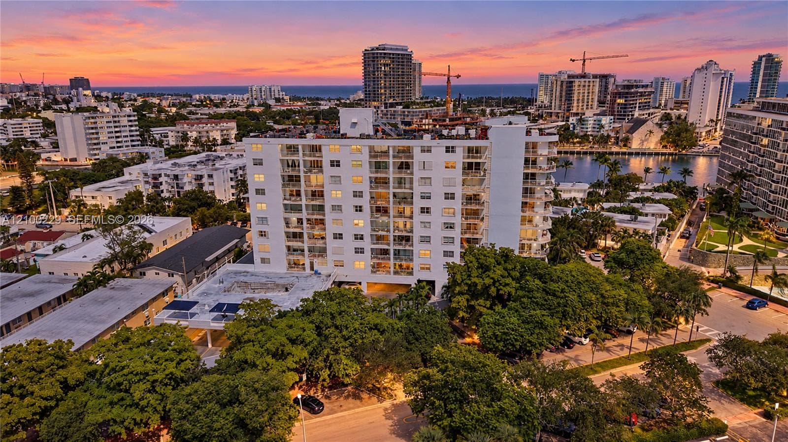 Mid-rise building featuring private balconies, an expansive roof deck, and mature landscaping, set against an urban skyline and coastal backdrop