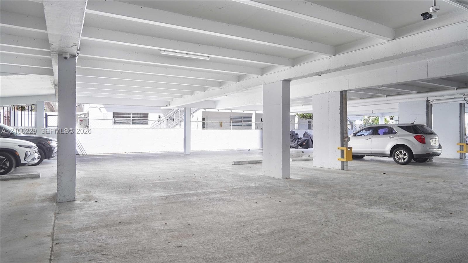 Covered parking area featuring concrete flooring, structural support columns, and overhead lighting
