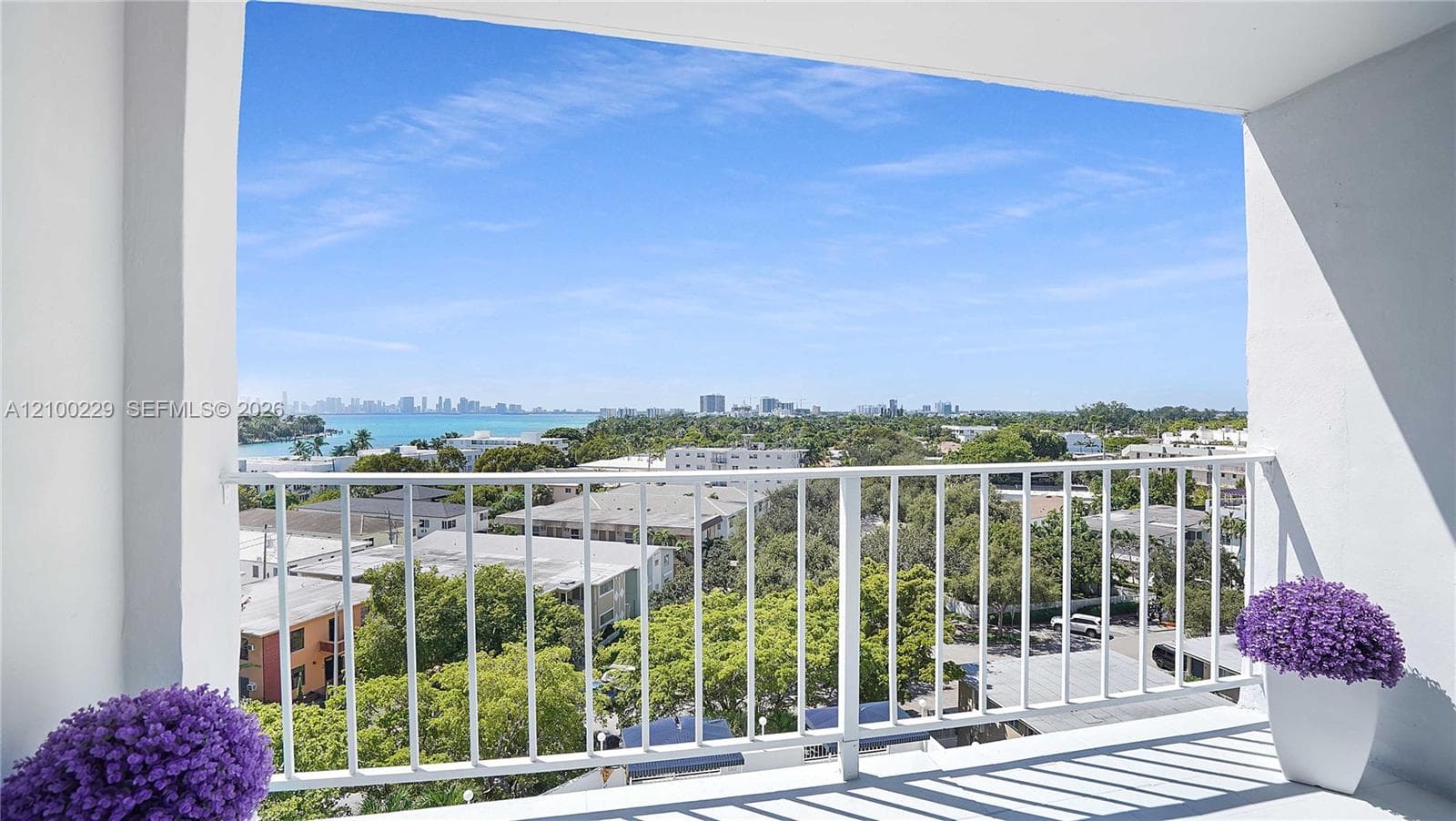 Covered balcony featuring white vertical railings, solid surface flooring, and a panoramic outlook of the surrounding cityscape and water