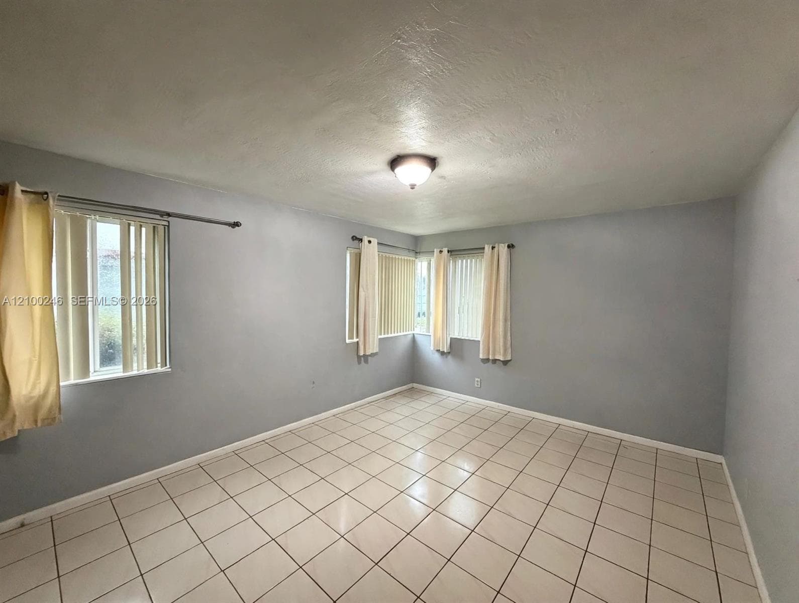 Interior room featuring light-toned tile flooring, neutral wall paint, three windows, and a flush-mount ceiling light fixture