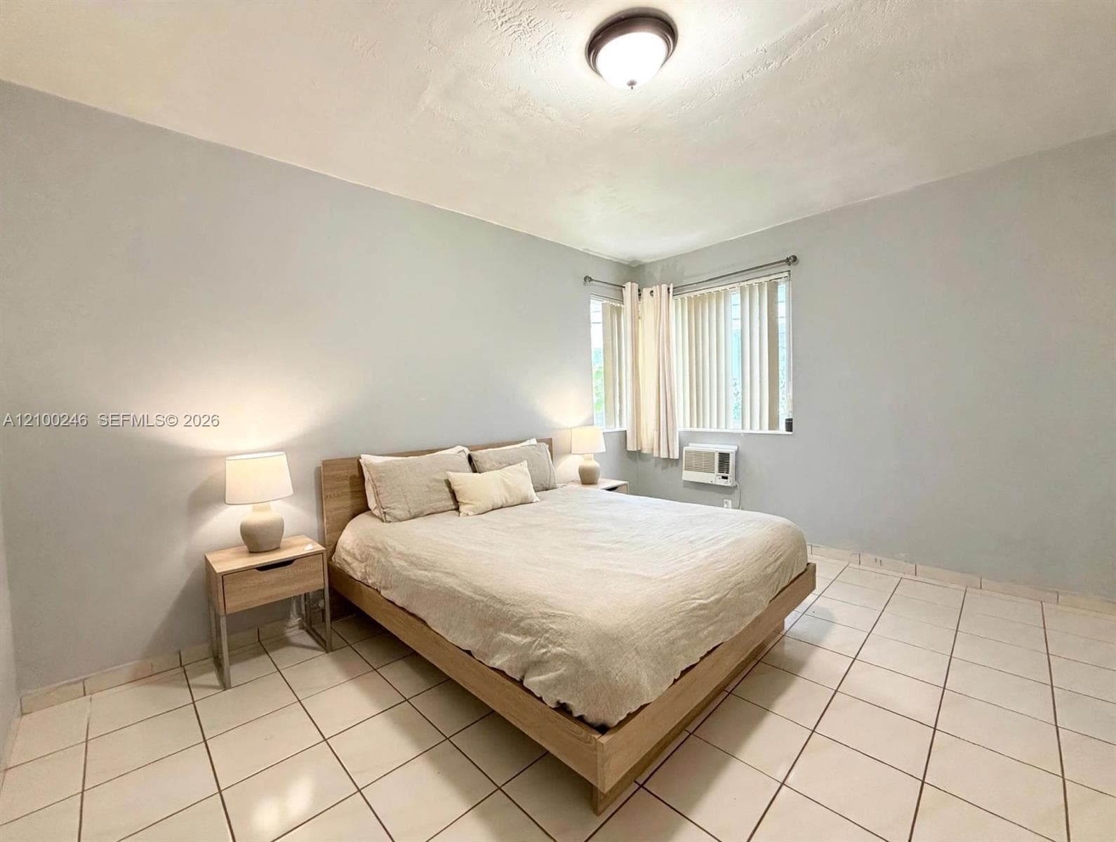 Neutral-toned walls, square ceramic floor tiling, and a ceiling-mounted light fixture, featuring corner windows and an integrated air conditioning unit