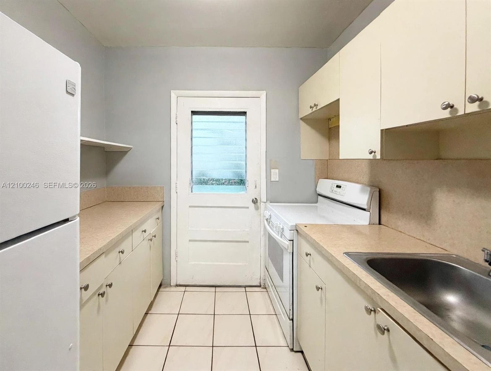 Kitchen featuring light-toned cabinetry, solid-surface countertops, tile flooring, and an exterior door with integrated glass panel