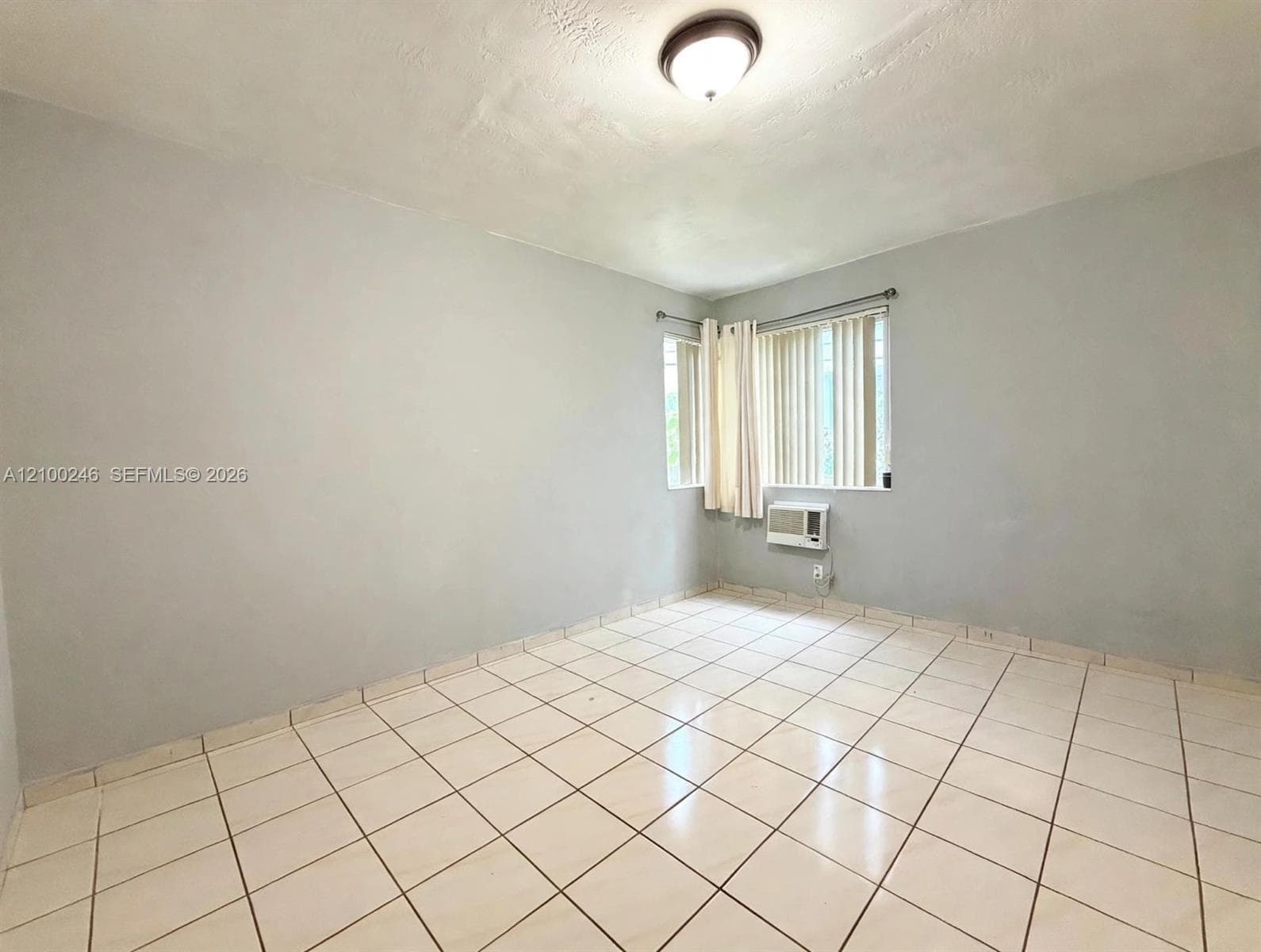 Neutral-toned interior space featuring tile flooring, a corner window configuration, and a wall-mounted air conditioning unit