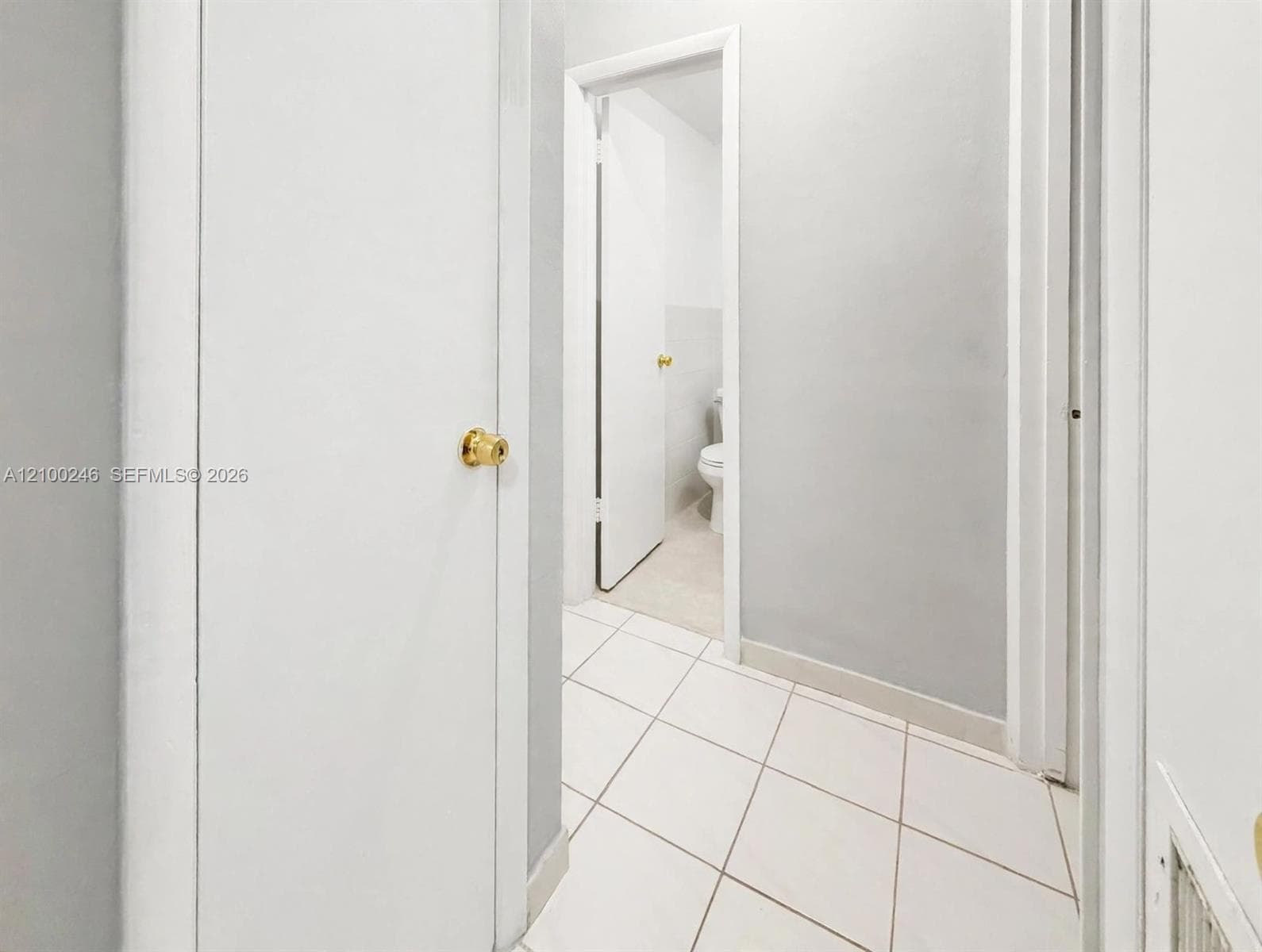 Interior hallway featuring neutral-toned walls, white tile flooring, and solid-core doors with gold-toned hardware