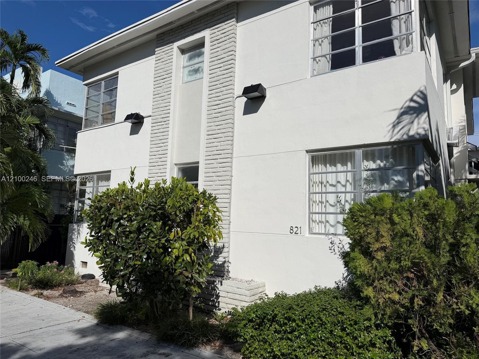 Two-story stucco exterior featuring a central vertical brick masonry element, multi-pane windows, and exterior wall-mounted lighting