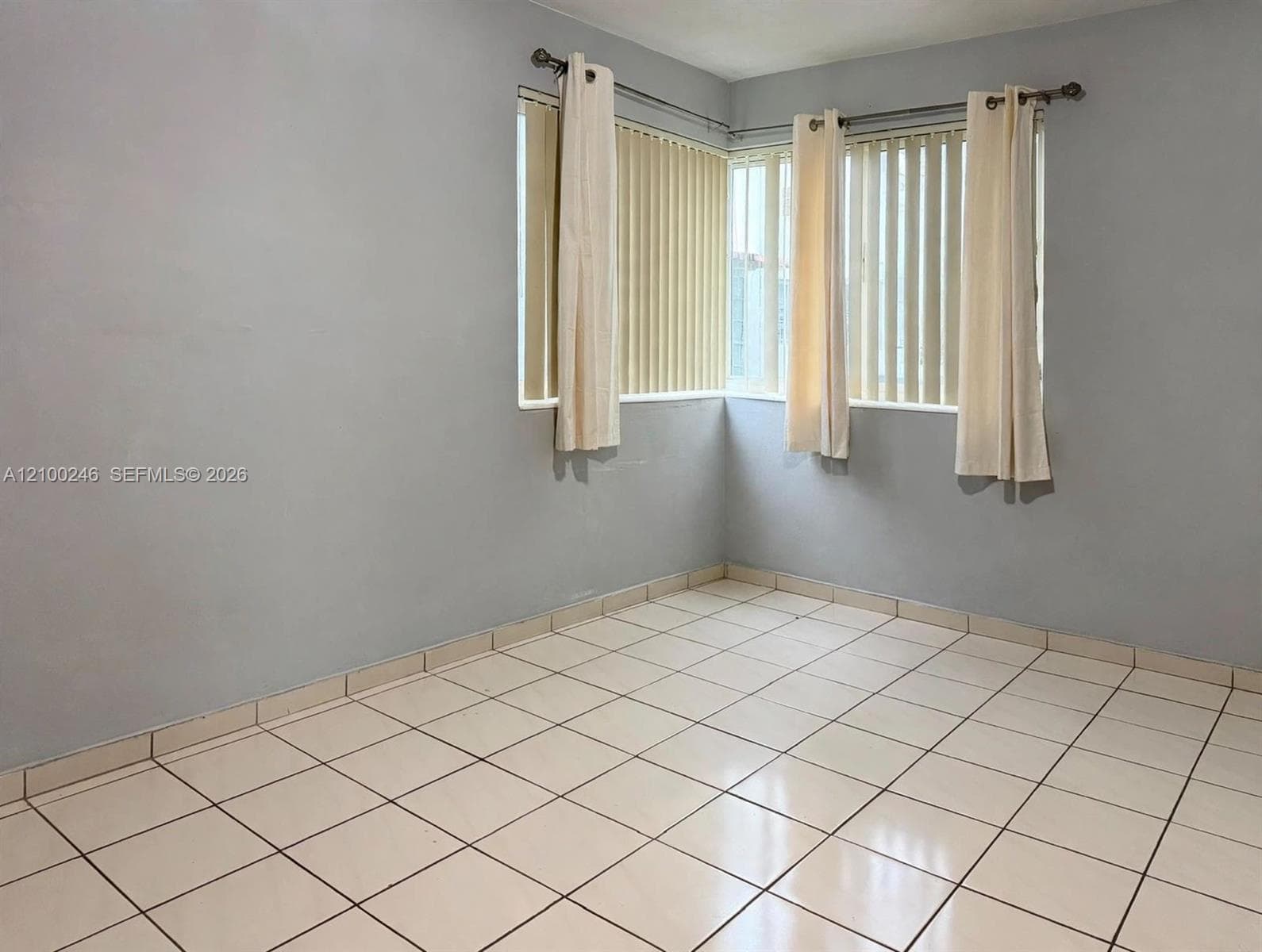 Room featuring white ceramic tile flooring and corner windows with vertical blinds