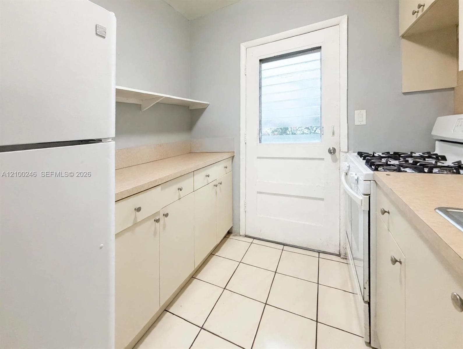 Kitchen featuring light-toned cabinetry, solid surface countertops, ceramic tile flooring, and an exterior door with a glass pane