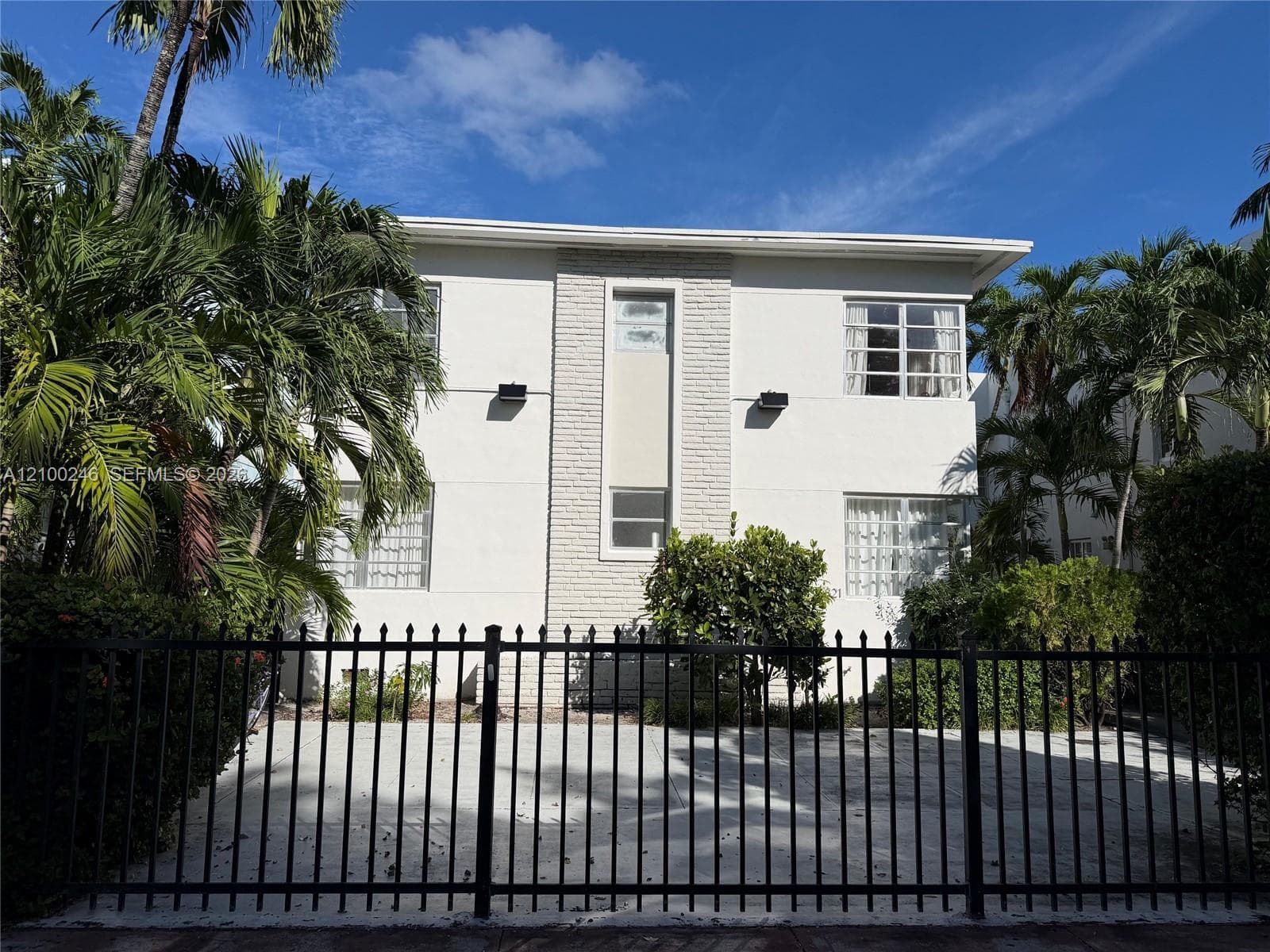 Two-story exterior featuring light-toned stucco, vertical brick accent detailing, multi-pane windows, and a metal perimeter fence