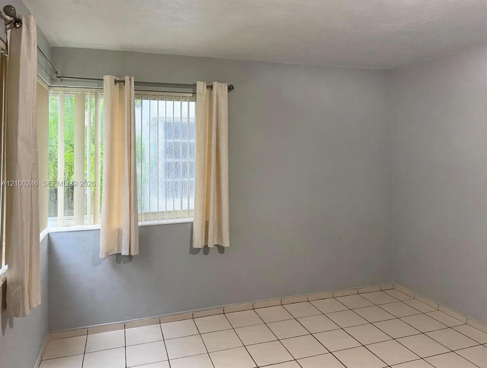 Interior space featuring light gray walls, large-format ceramic tile flooring, and windows with vertical blind treatments