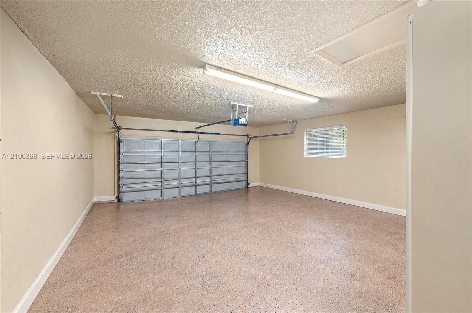 Garage featuring a sectional overhead door, epoxy-finished flooring, flush-mount fluorescent lighting, and a window with exterior light exposure