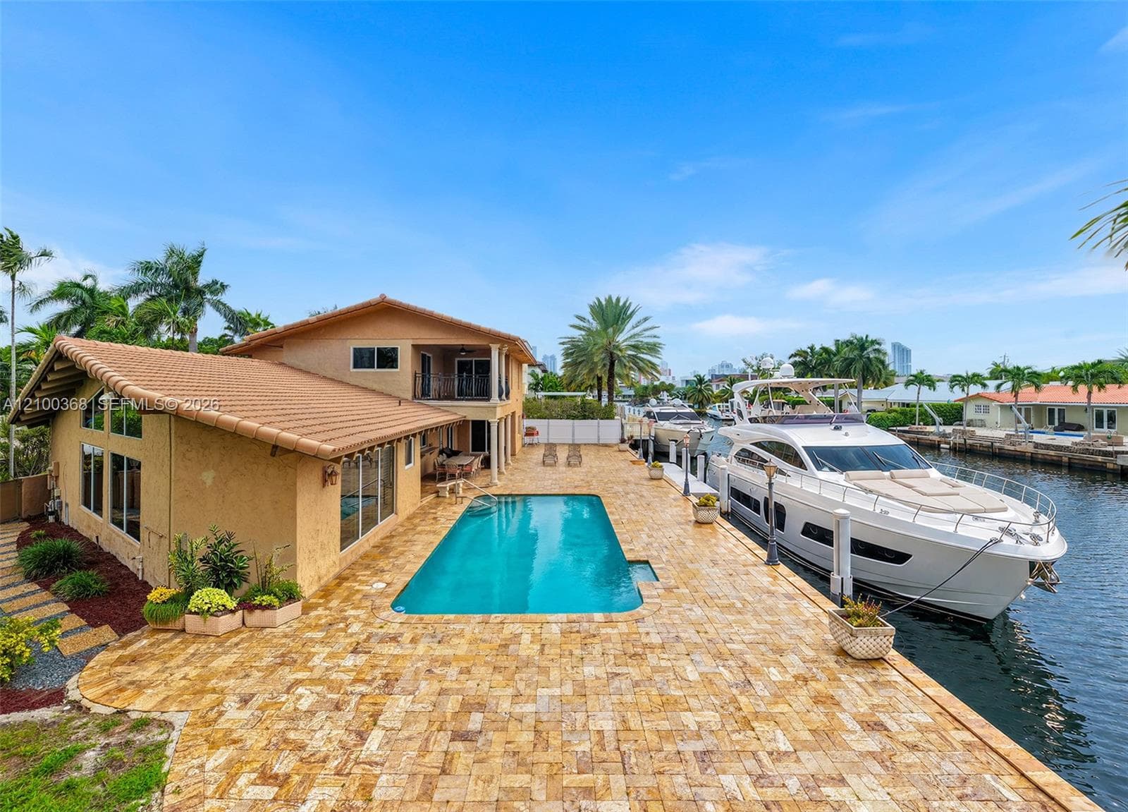 Waterfront residence featuring a private boat dock, in-ground swimming pool, expansive stone-paver patio, and two-story stucco exterior with a tile roof