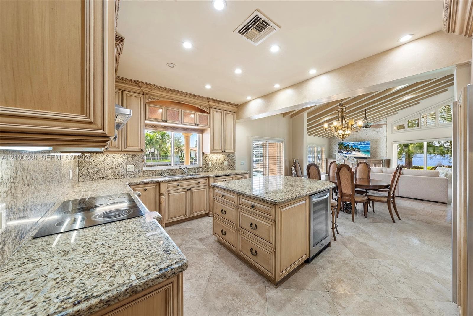 Kitchen featuring natural stone countertops, custom cabinetry, a center island with built-in wine refrigeration, tile flooring, and recessed lighting