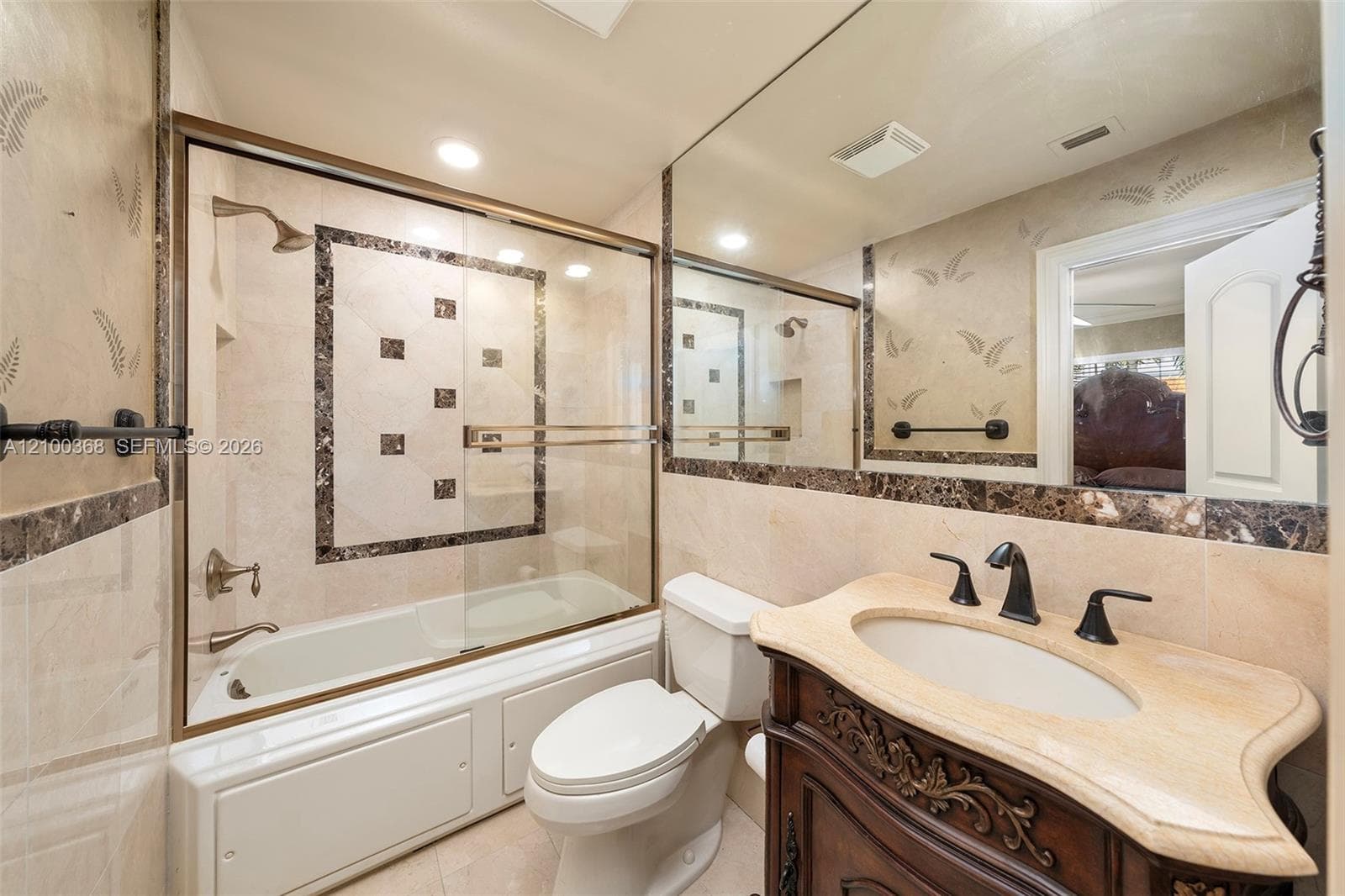 Bathroom featuring a custom wood vanity with stone countertop, undermount sink, brass-finished faucet, and large wall-to-wall mirror