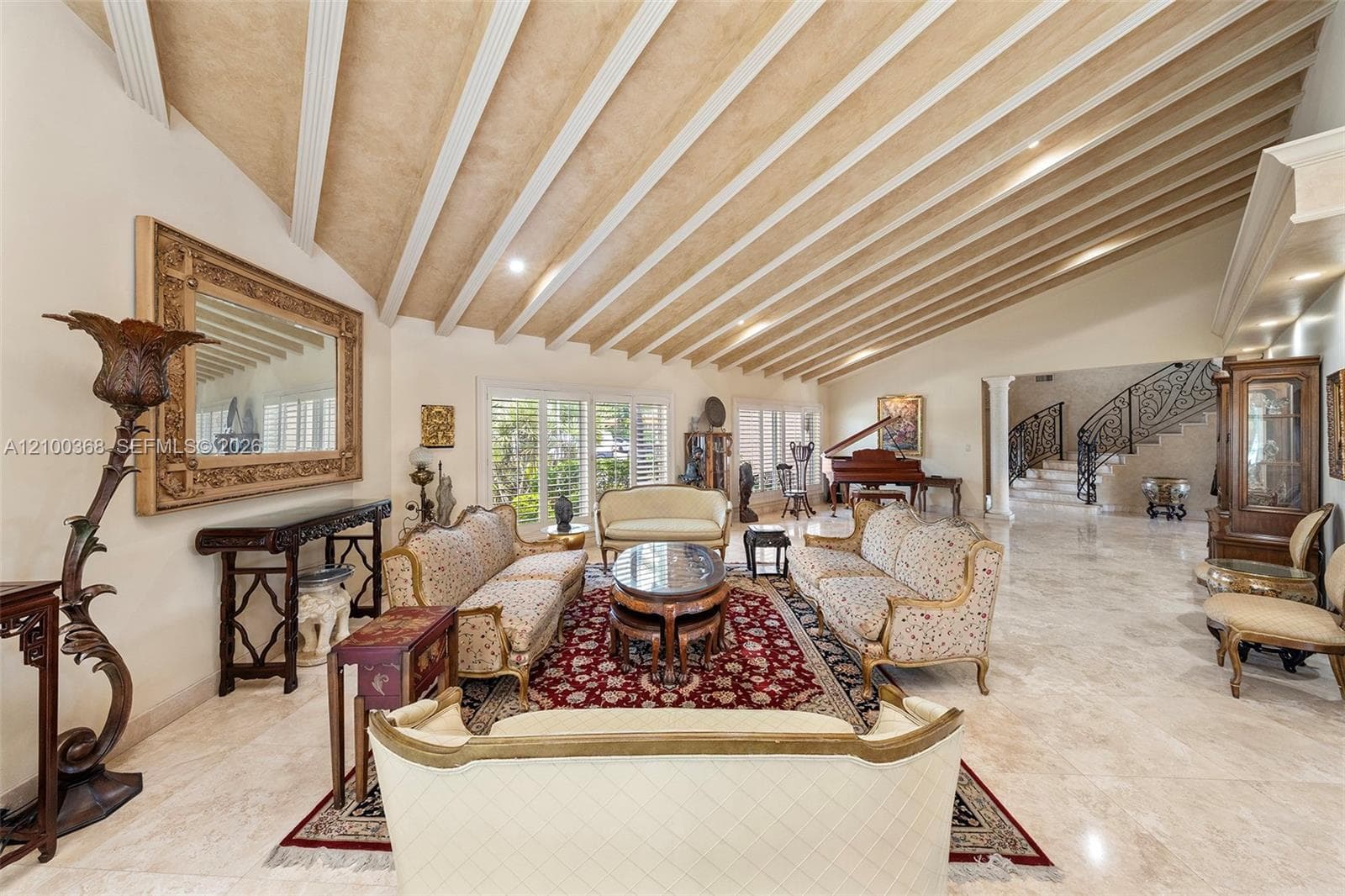Vaulted ceiling with decorative wood beams, stone flooring, recessed lighting, and ornate staircase with decorative metal railing