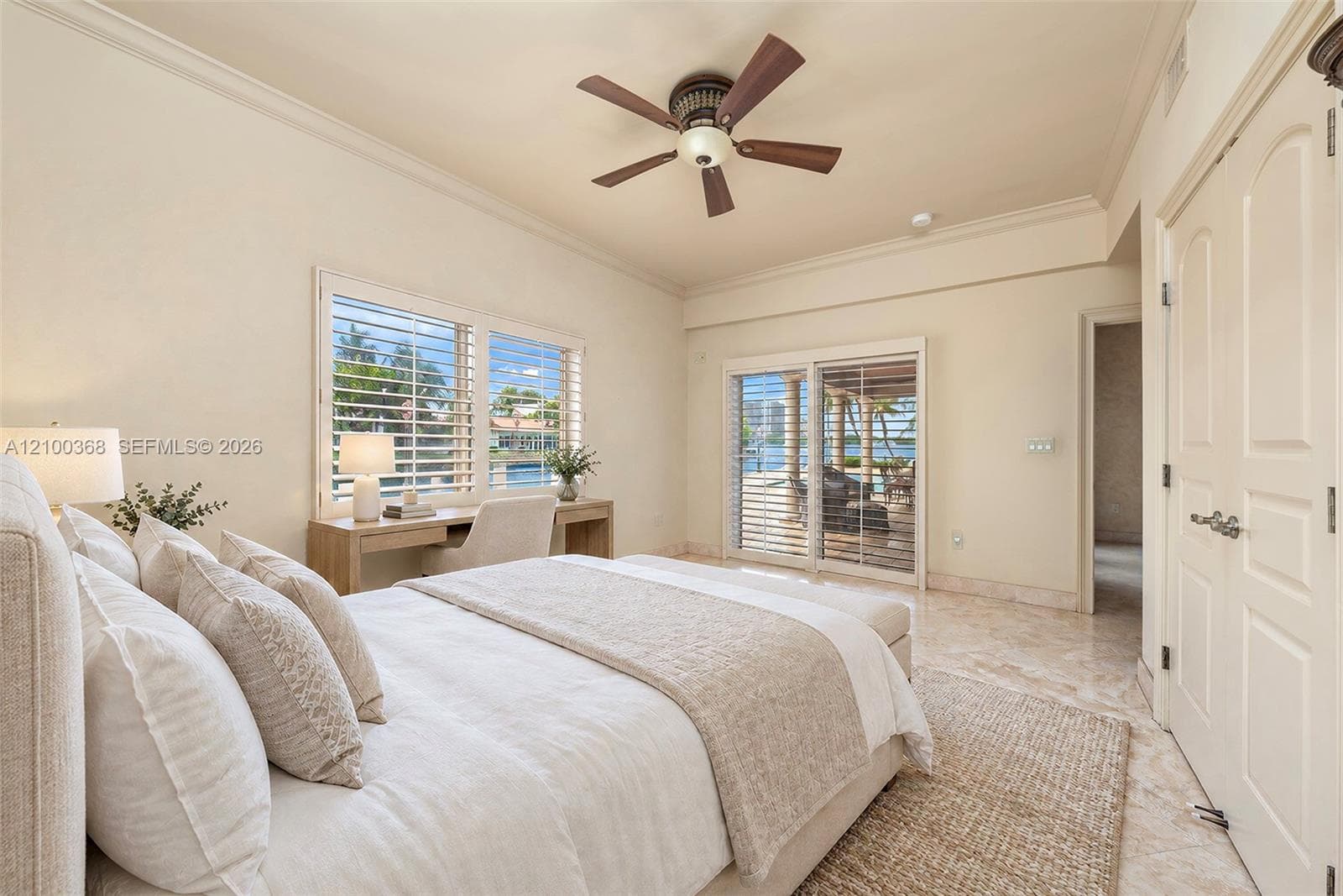 Room featuring stone-finish tile flooring, ceiling fan, crown molding, built-in desk, and sliding glass doors