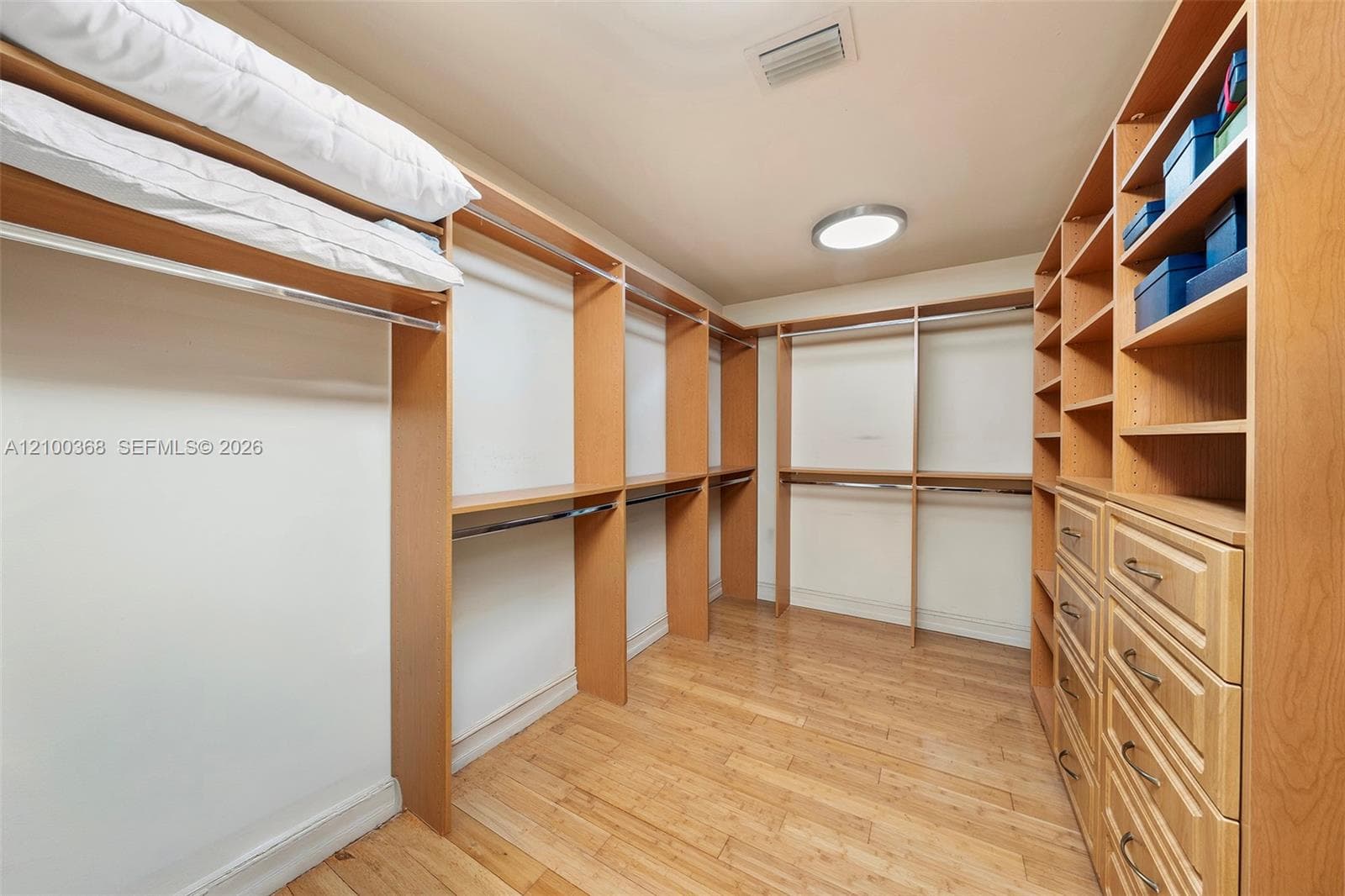 Walk-in closet featuring custom wood cabinetry, extensive shelving, hanging rods, integrated drawer units, and wood-finish flooring