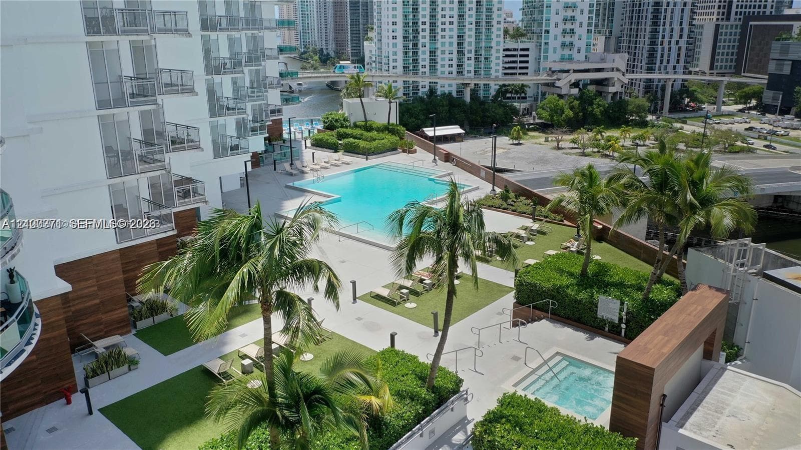 Outdoor swimming pool and spa area featuring concrete decking, manicured landscaping, mature palm trees, and wood-finish architectural accents
