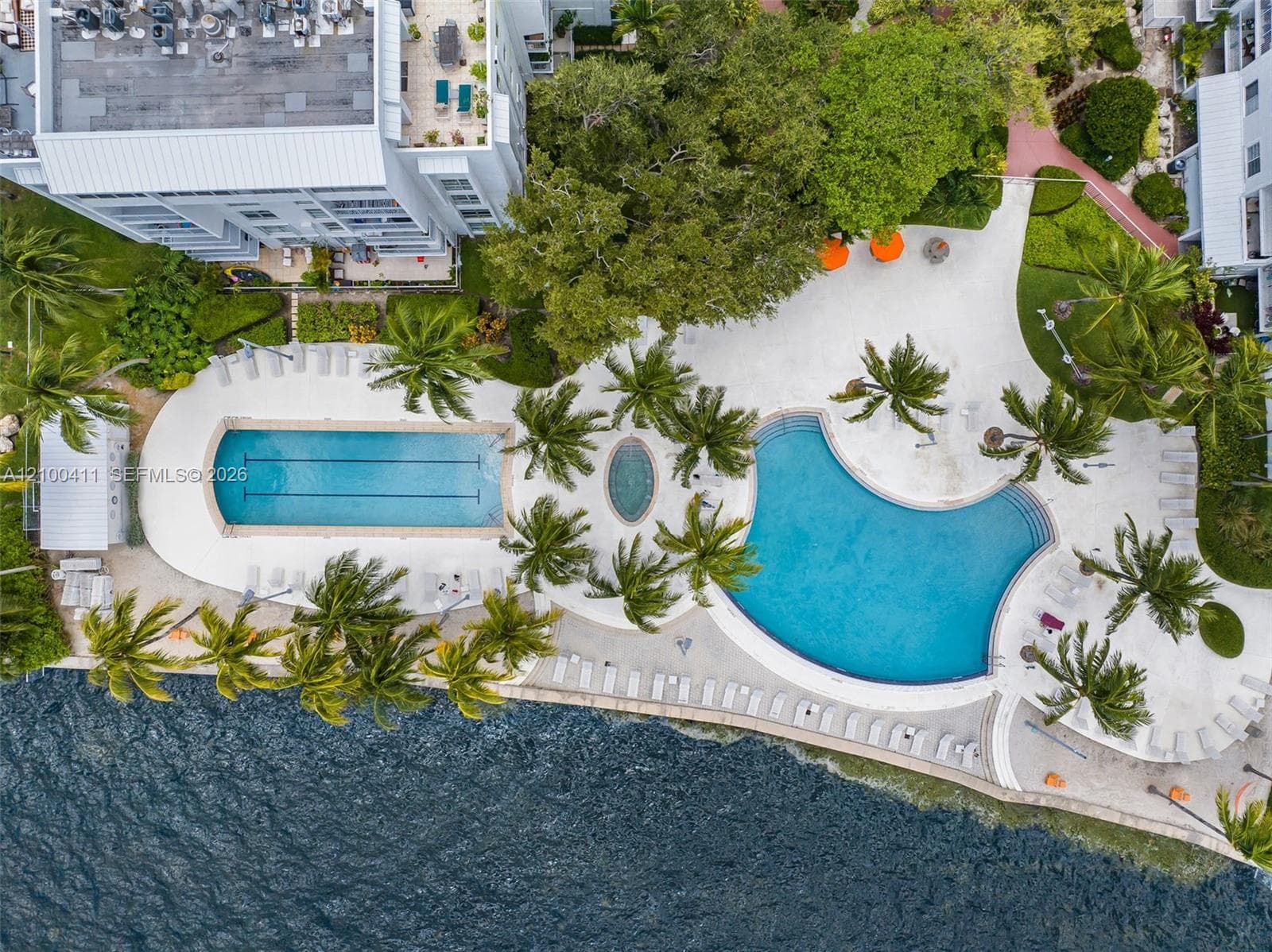 Waterfront community amenities featuring a lap pool, a free-form pool, a spa, expansive sun decks, and mature tropical landscaping