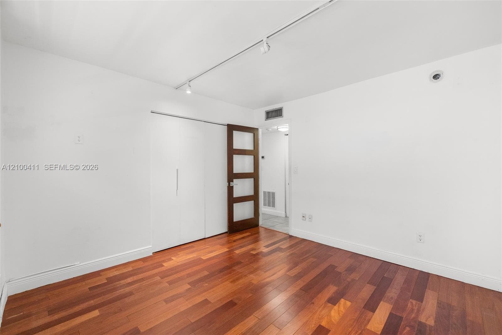 Room featuring wood-finish flooring, white walls, track lighting, built-in sliding closet doors, and a four-panel glass-inset door