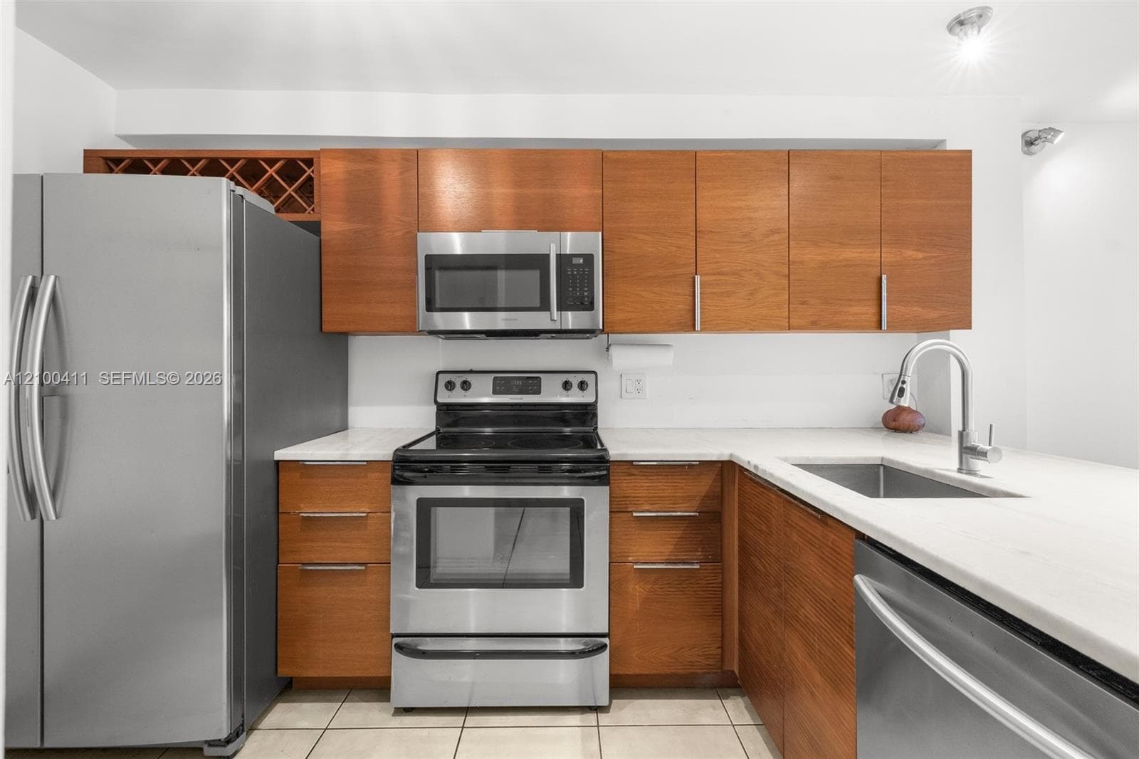 Kitchen featuring wood-finish cabinetry, built-in wine storage, stone-finish countertops, stainless steel appliances, and a stainless steel undermount sink with a gooseneck faucet