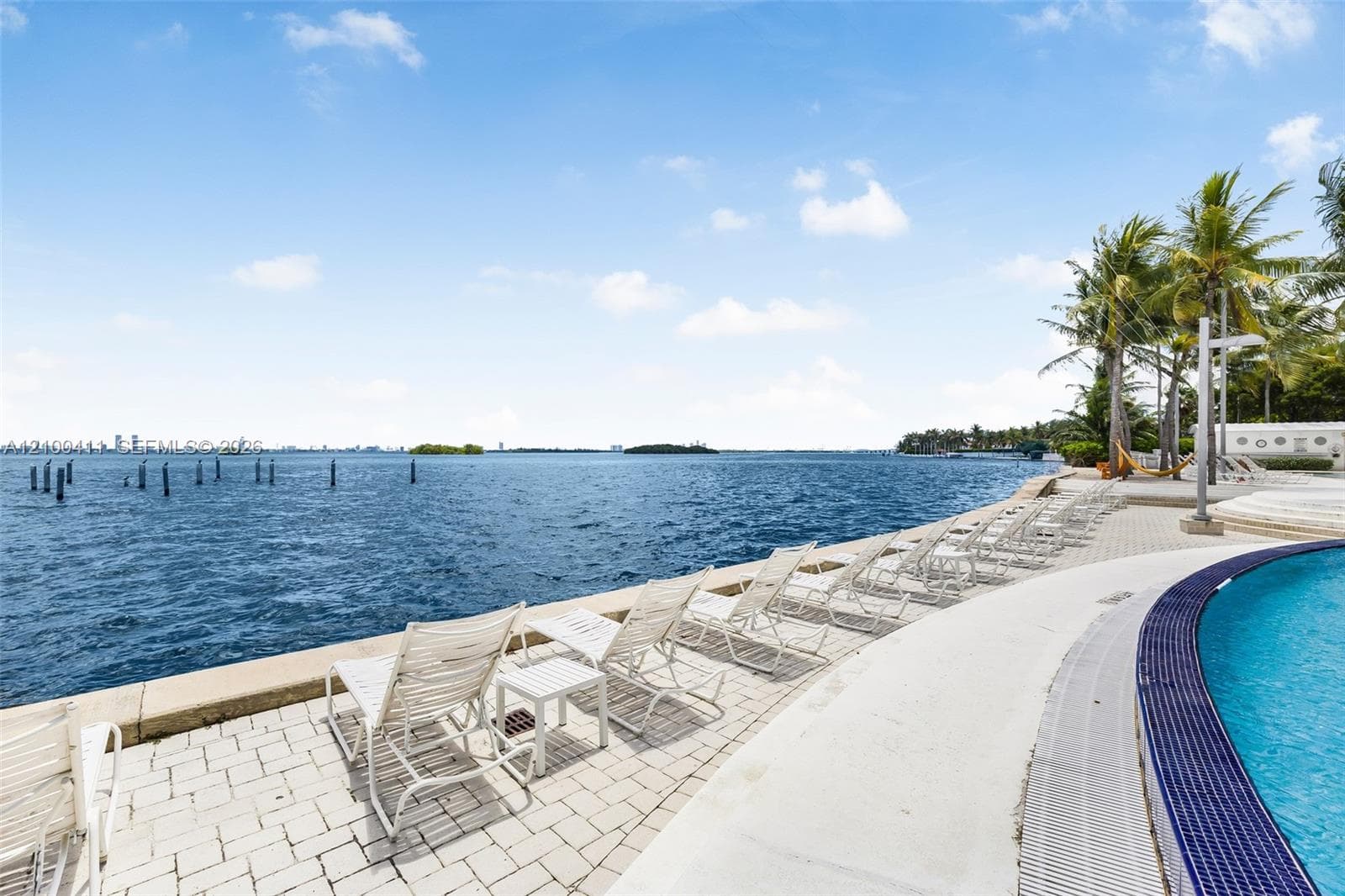 Waterfront pool area featuring a paved deck, deep-blue tiled pool edge, and direct open-water access