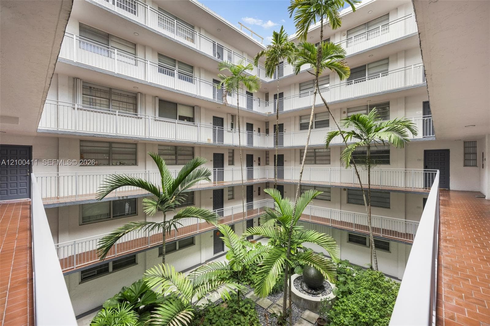 Multi-level open-air central courtyard featuring tile flooring, metal railings, mature palm trees, and a decorative stone fountain