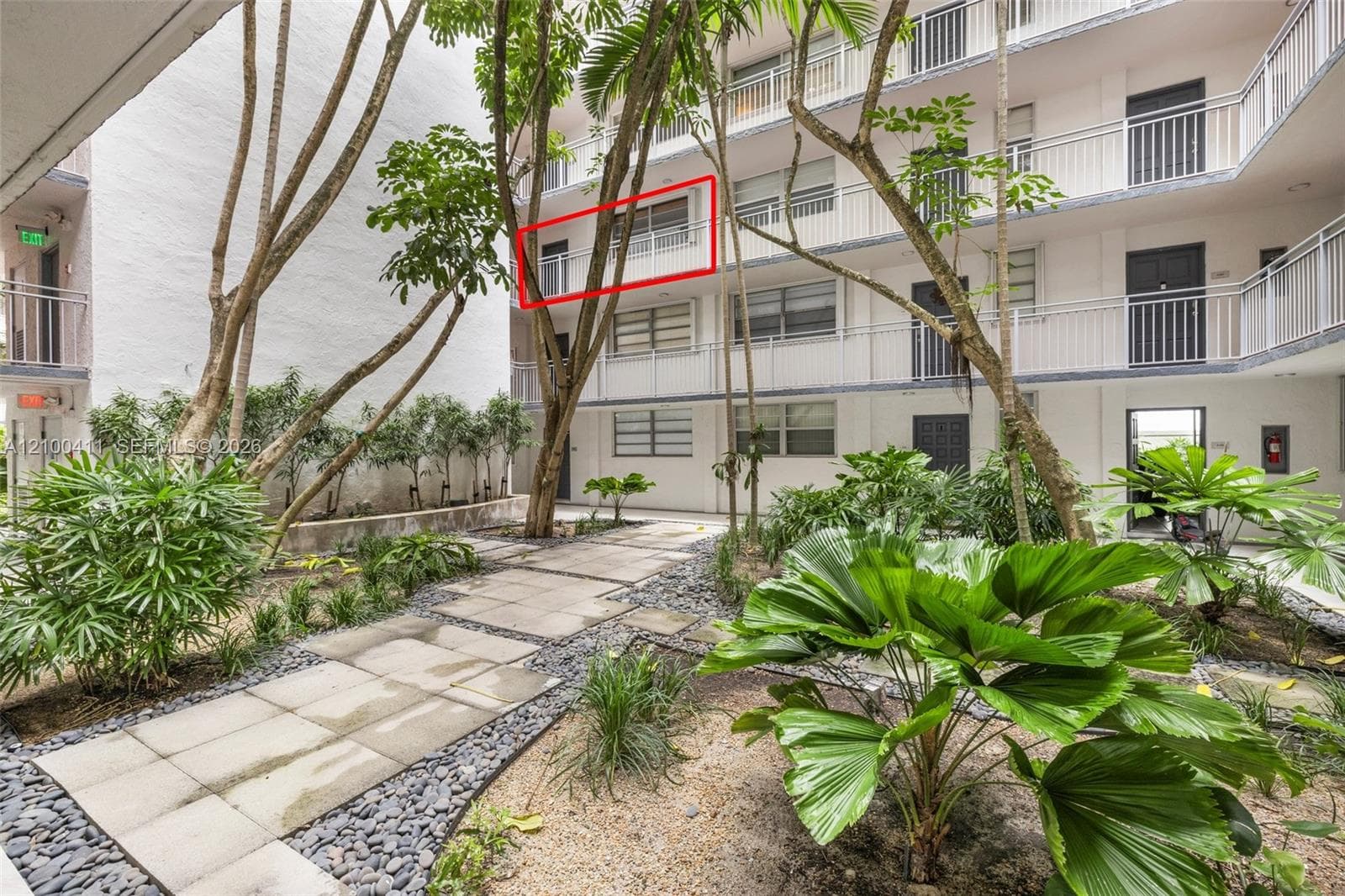 Multi-story exterior featuring a private balcony, paved walkway, decorative stone accents, and mature tropical landscaping