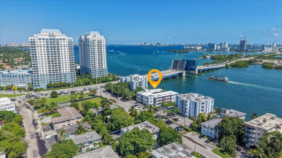 Aerial perspective of coastal multi-story residential building featuring proximity to waterfront, bridge access, and mature landscaping
