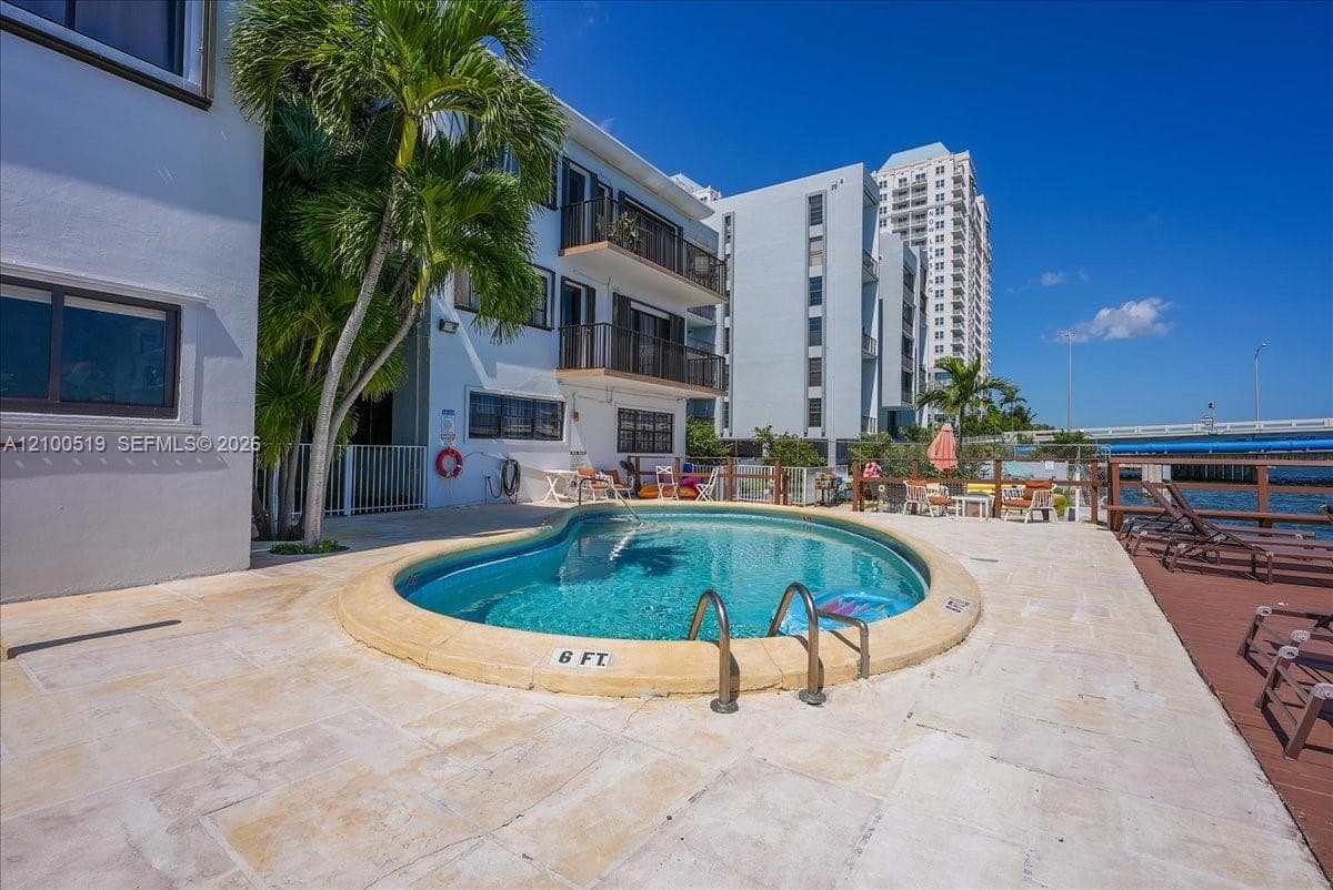 In-ground swimming pool with stone coping, surround of light-toned natural stone pavers, multi-story structure with private balconies, and waterfront positioning