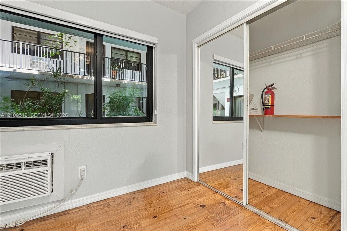 Room featuring wood-finish flooring, a black-frame window, and a closet with sliding mirrored doors