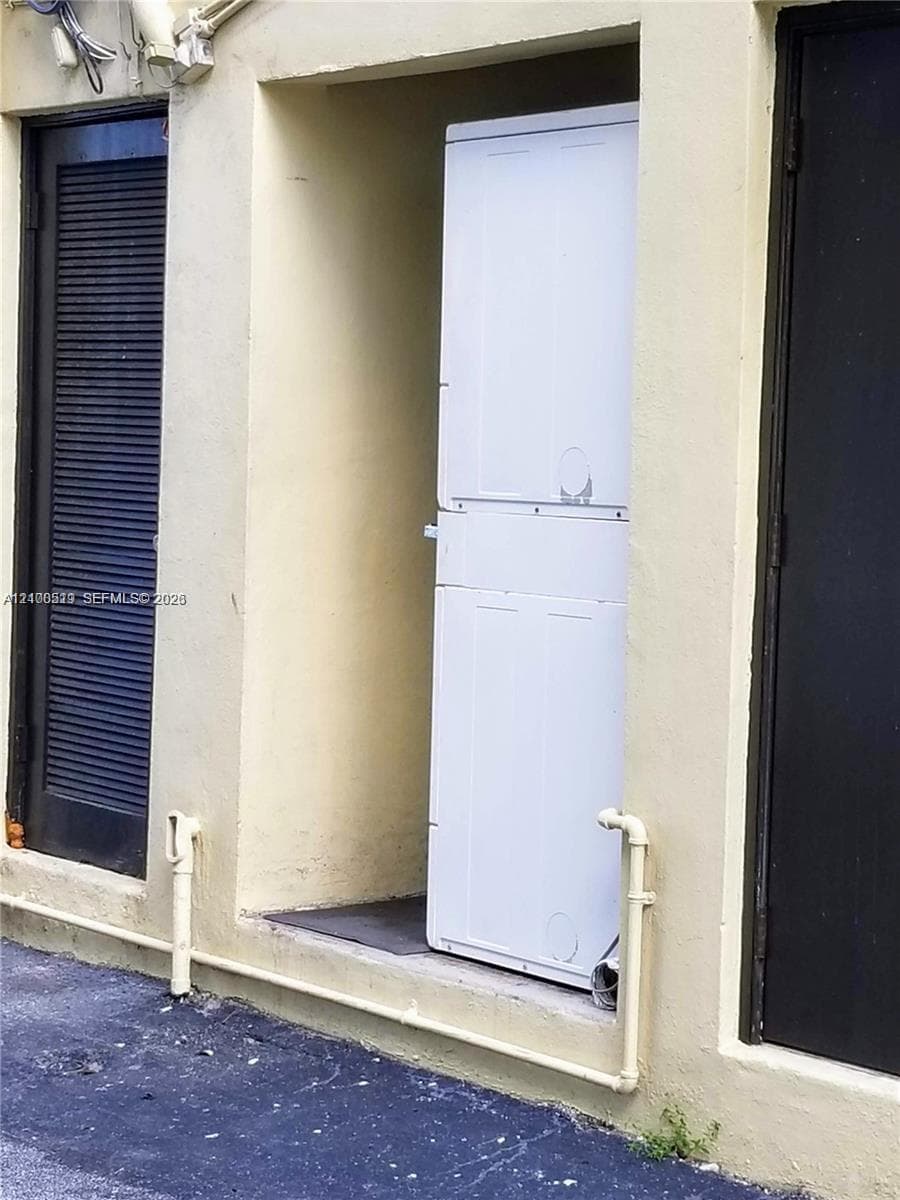 Stacked laundry unit housed within a recessed exterior alcove, featuring dual dark-toned louvered doors and exposed utility piping