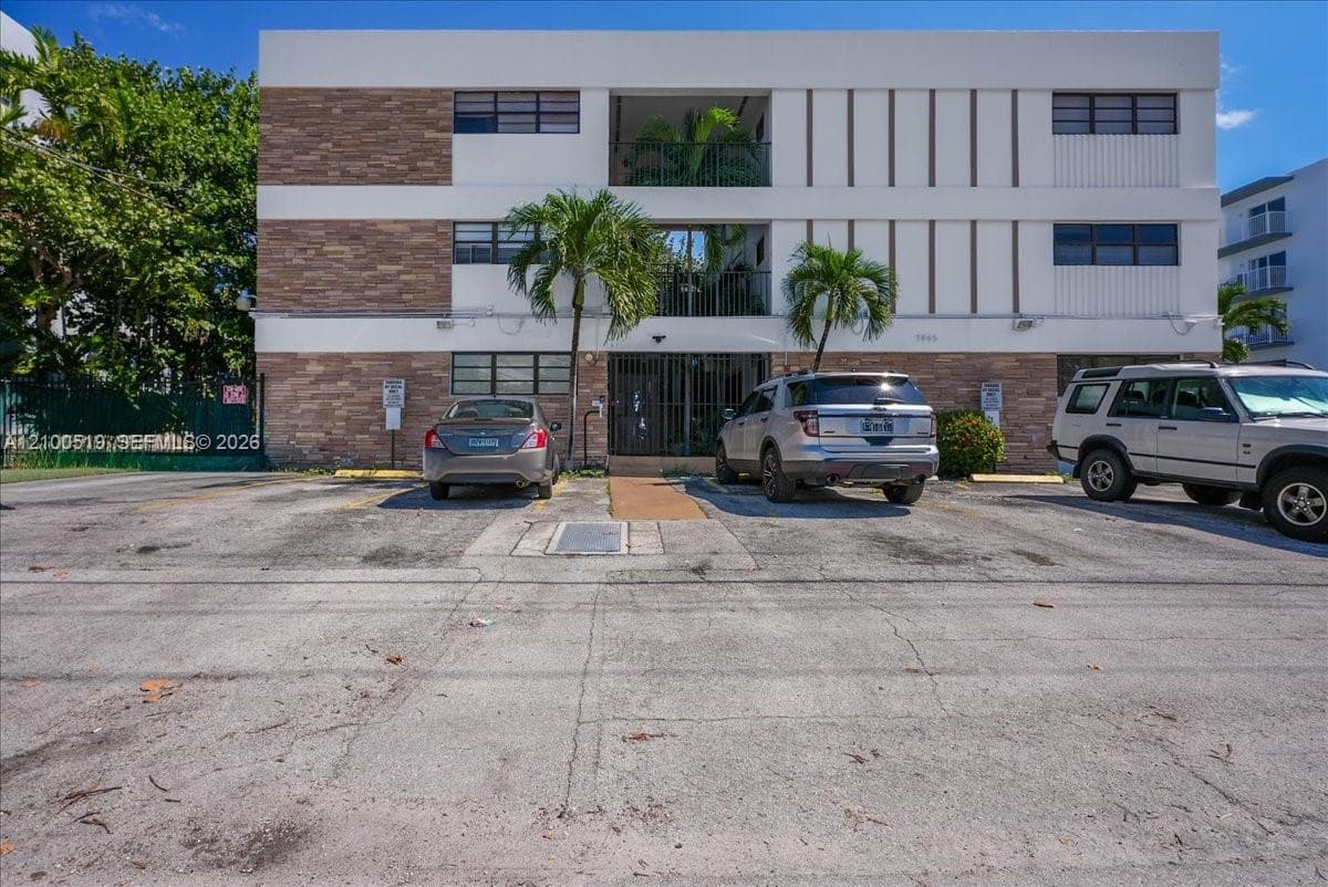 Three-story building exterior featuring stone masonry, vertical siding, private recessed balconies, and paved surface parking