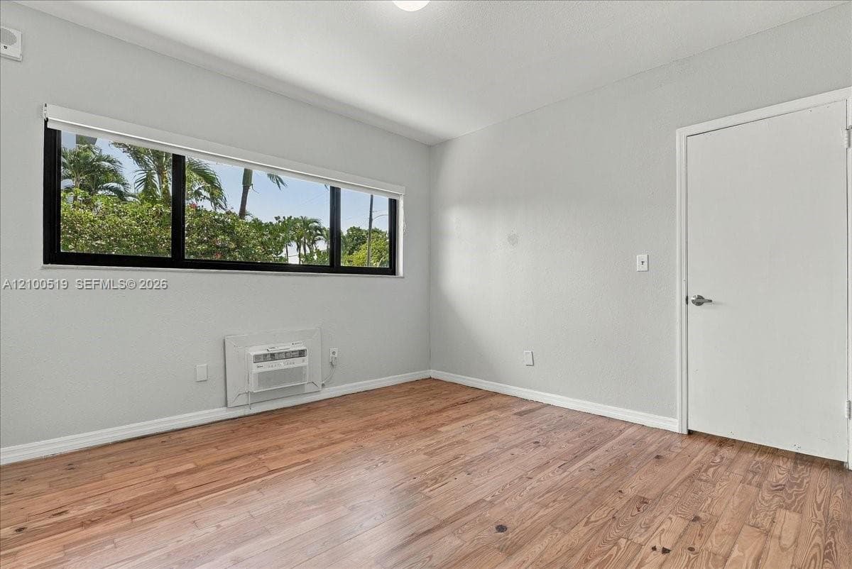 Room featuring wood-finish flooring, a wide window with a black frame, and a wall-mounted climate control unit