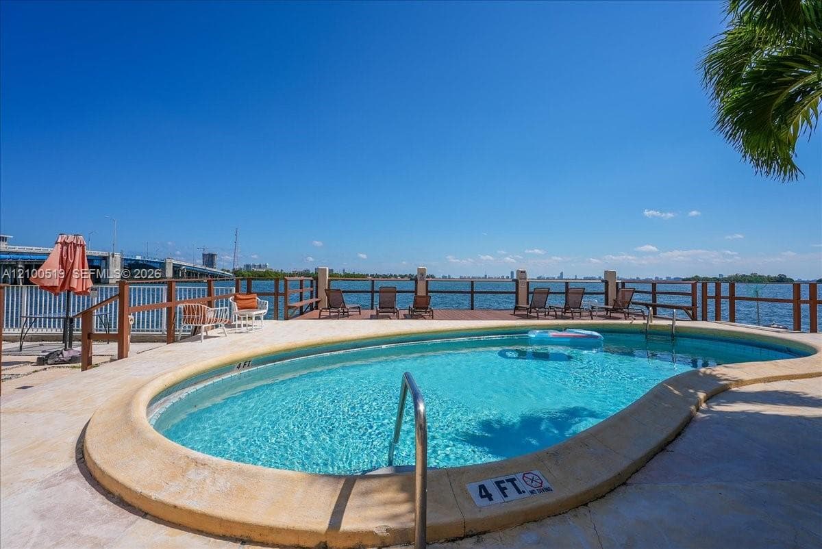 Freeform swimming pool with a rounded perimeter, stone-finish pool deck, and integrated metal handrail, featuring a waterfront wooden deck with a perimeter railing