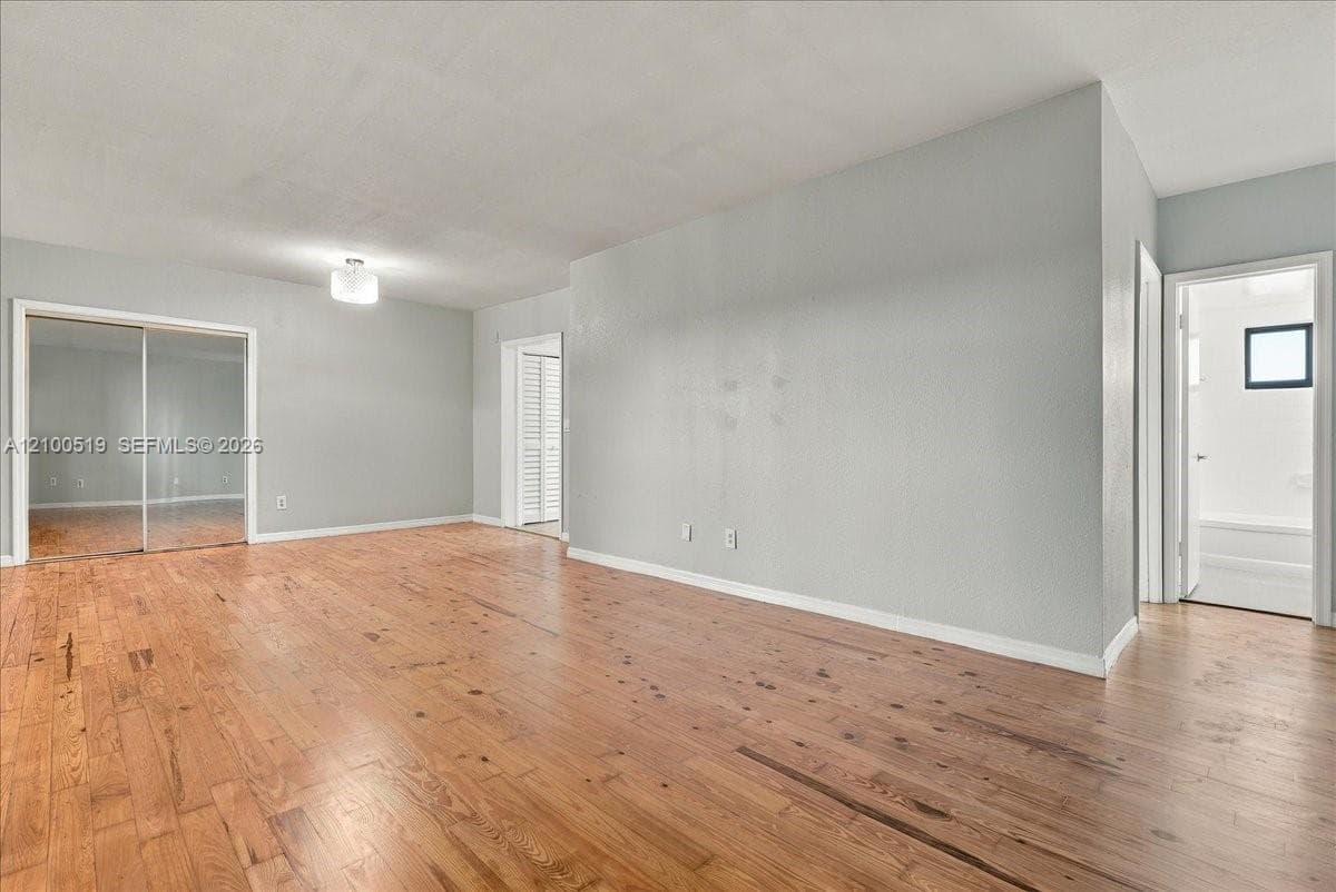 Interior space featuring wood-finish flooring, neutral wall tones, mirrored sliding closet doors, and an overhead light fixture