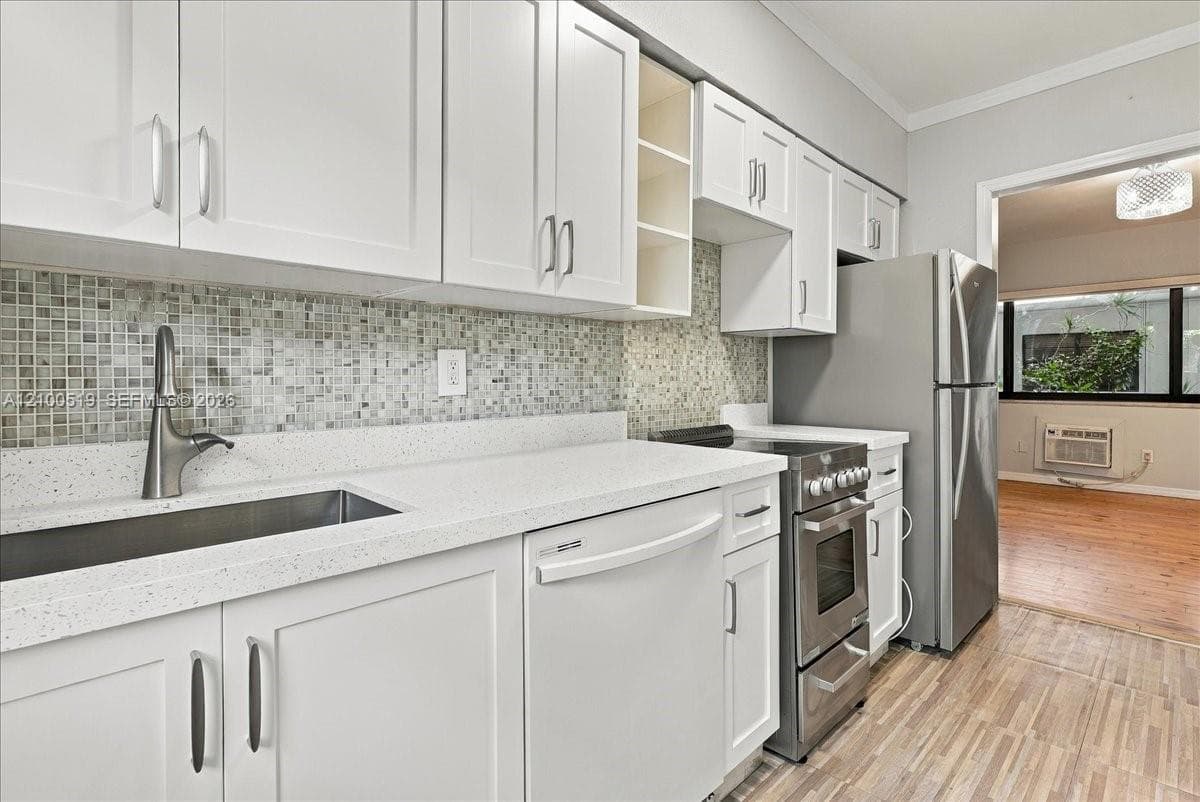 Kitchen featuring white shaker-style cabinetry, a mosaic tile backsplash, solid-surface countertops, an undermount stainless steel sink with a high-arch faucet, and stainless steel appliances
