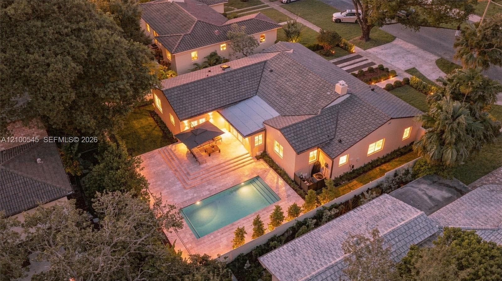 Single-story residence featuring a tile roof, an expansive stone-paved patio, a rectangular in-ground pool, and mature landscaping