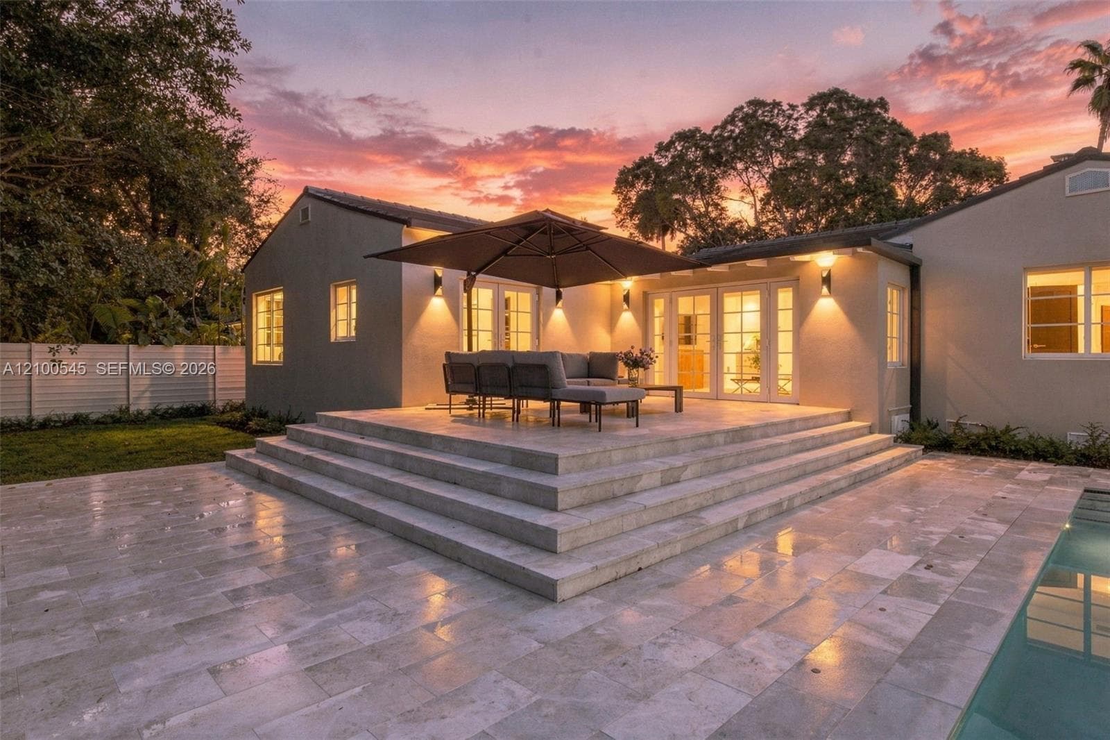 Rear exterior featuring a multi-level stone patio, built-in swimming pool, horizontal slat fencing, and double-glass paneled doors