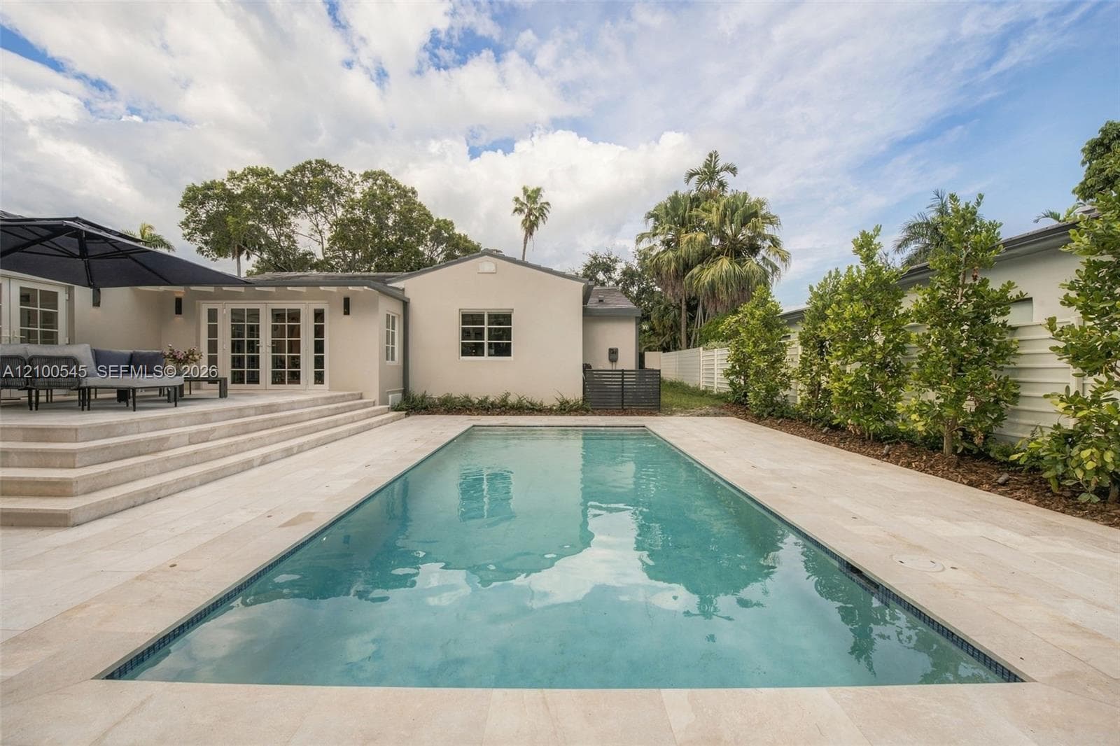 Rectangular inground pool with stone tile surround, tiered concrete patio steps, multi-lite French doors, and perimeter privacy fencing