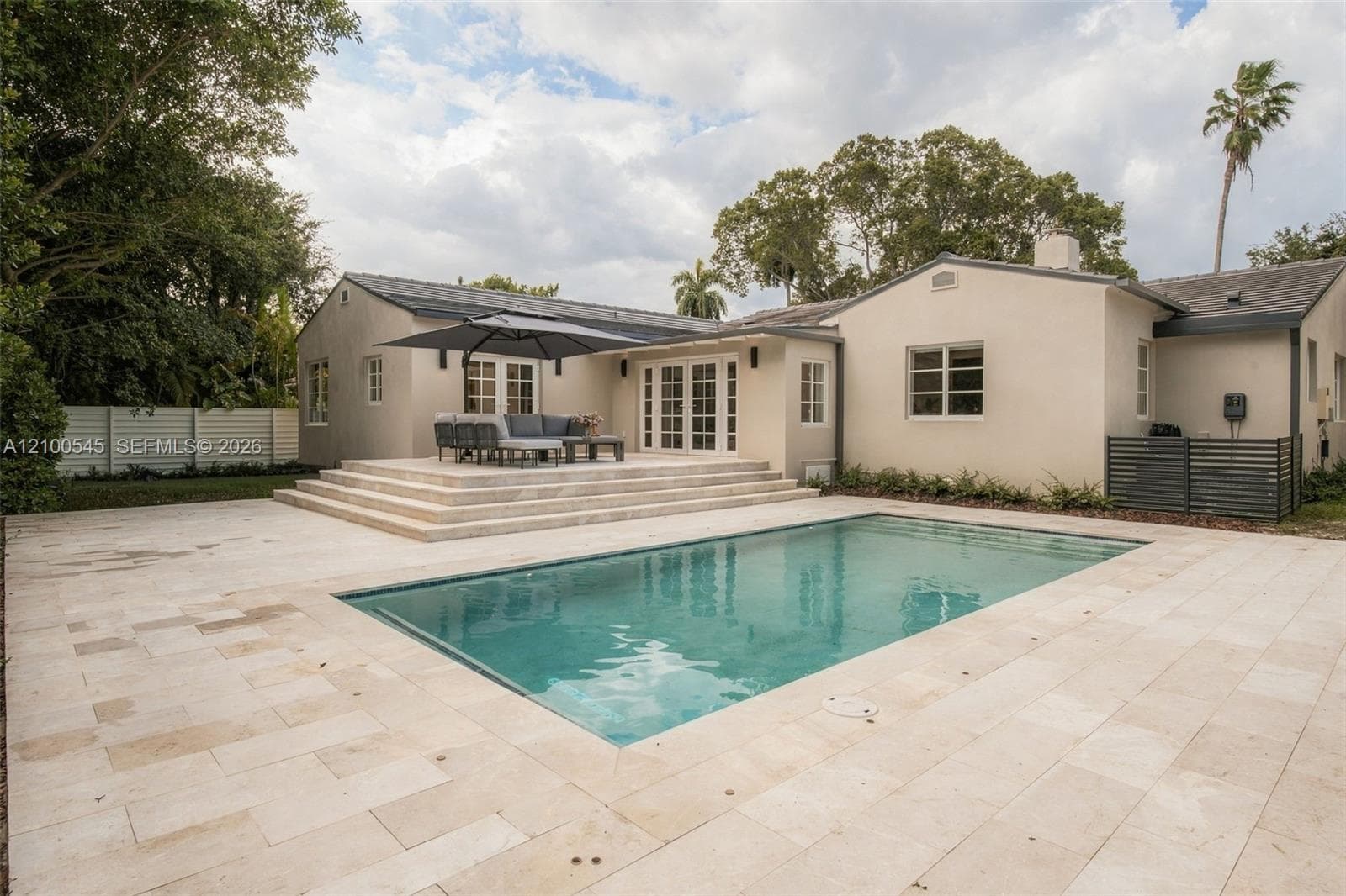 Rectangular in-ground swimming pool featuring stone surround decking, multi-tiered stone platform, and exterior French doors
