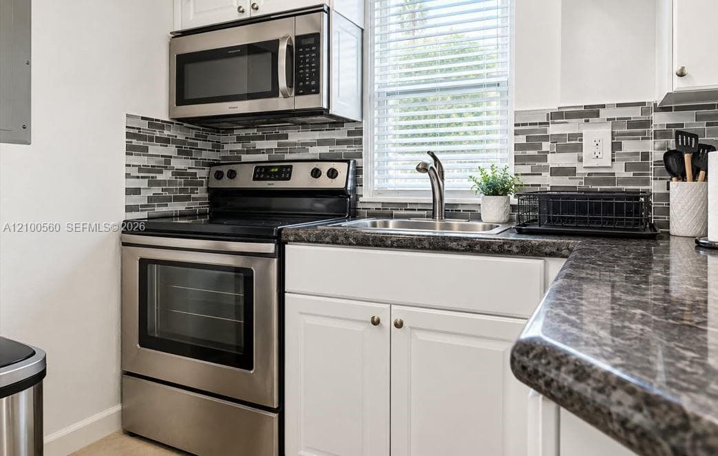 Kitchen featuring white cabinetry, dark stone-finish countertops, stainless steel appliances, and a glass-tile backsplash