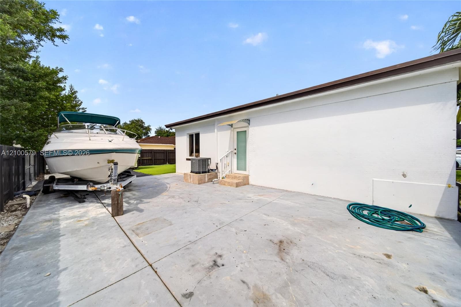 Concrete side yard featuring a white exterior finish, metal door awning, and perimeter wood fencing